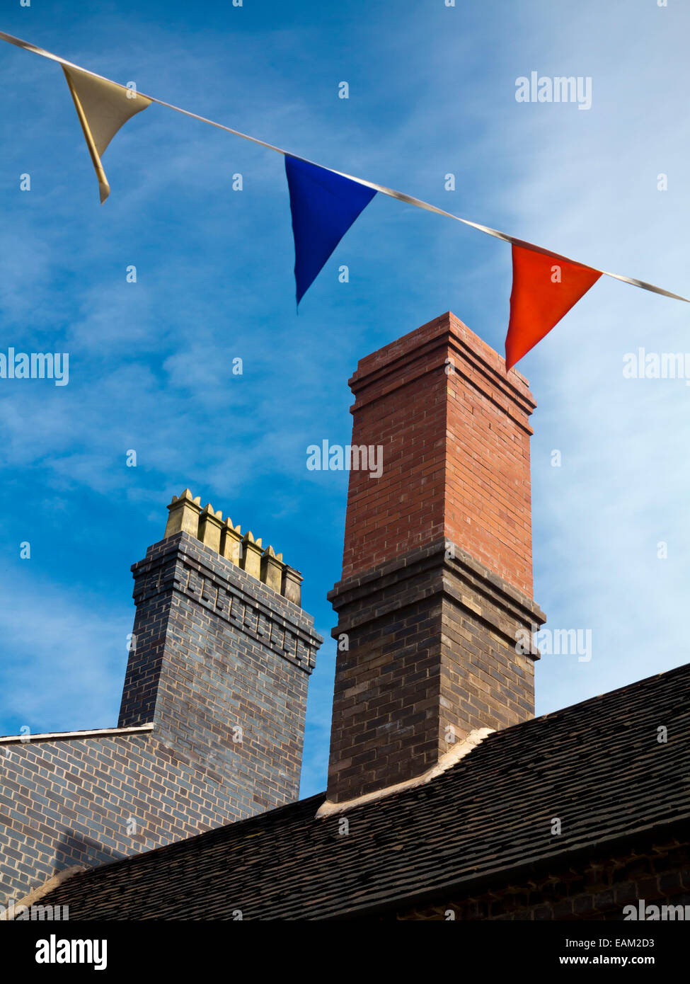 Bunting flags flying on a street with roof and chimneys behind and blue sky in background Stock Photo