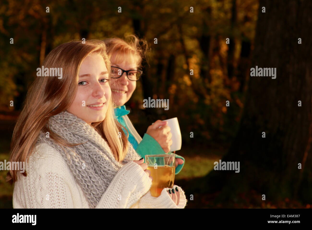 Daughter and mother drink tea in autumn park, horizontal Stock Photo