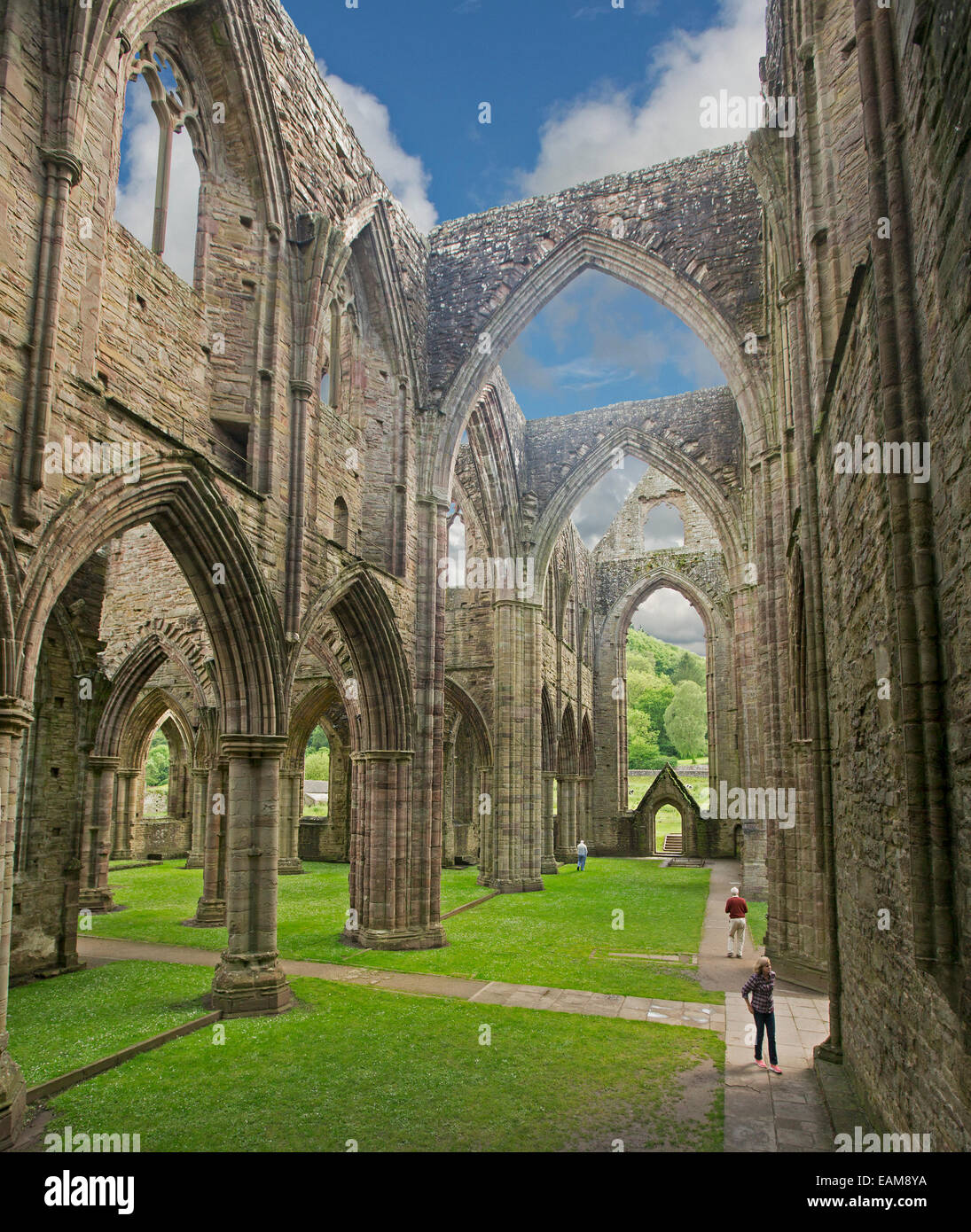 Spectacular remains of 12th century Tintern abbey with 2 people dwarfed by its immense walls and arches that rise into blue sky Stock Photo