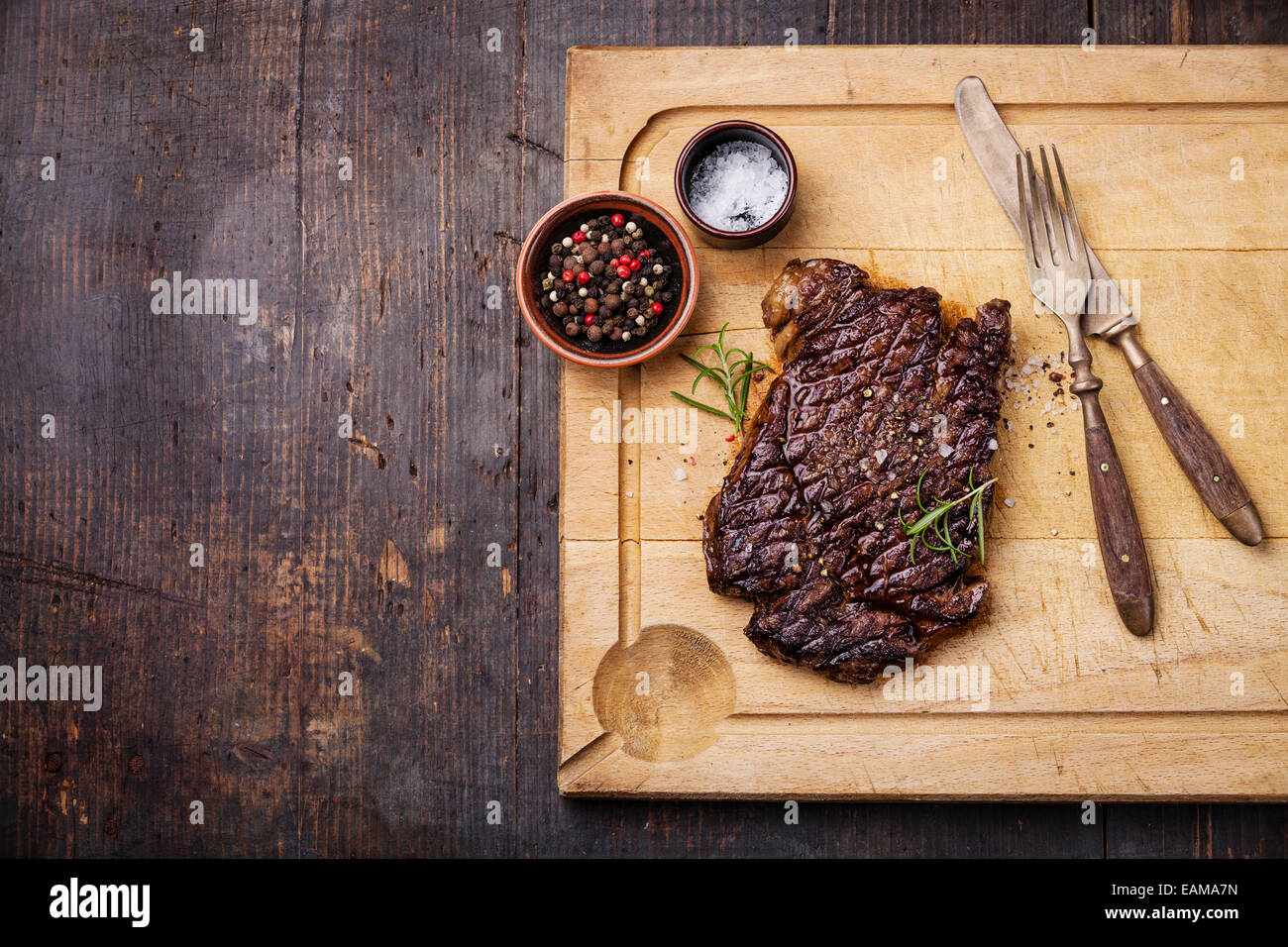 Grilled Ribeye Steak with salt and pepper on meat cutting board on dark