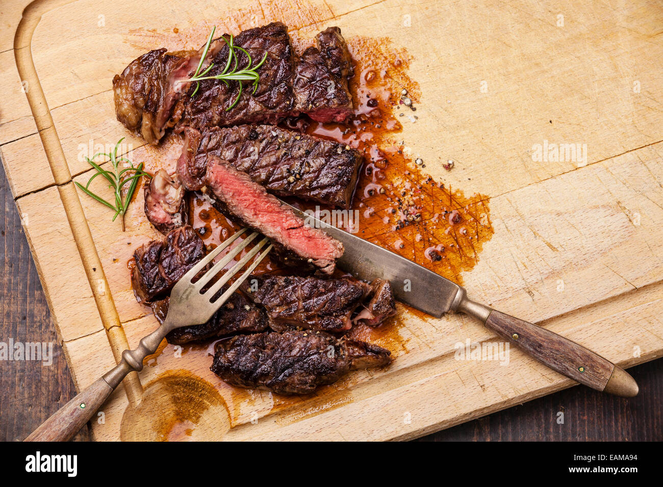 Grilled Ribeye Steak with with knife and fork on meat cutting board on