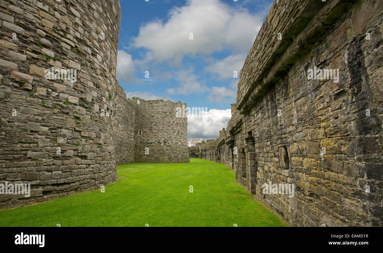 View of vast interior of historic Beaumaris castle with immense stone walls shading lawns and under blue sky in Wales Stock Photo