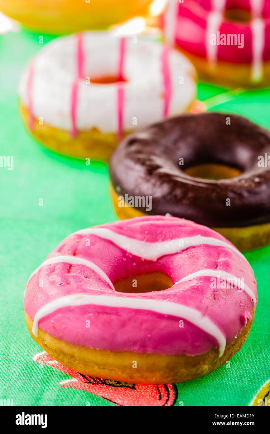 some delicious and colorful donuts on a green ornated tablecloth Stock Photo
