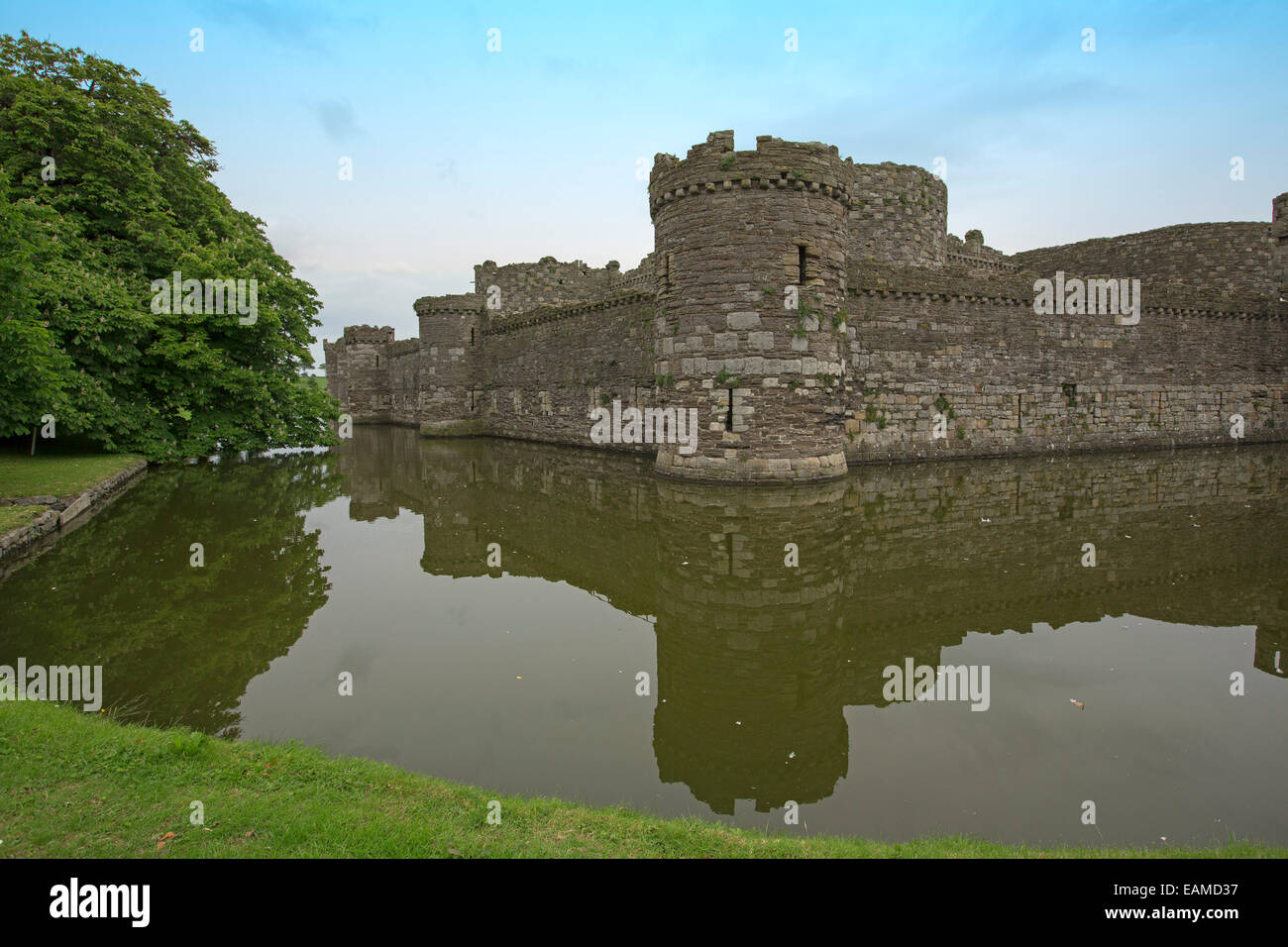 Spectacular 13th century Beaumaris castle  with high walls & towers reflected in calm water of moat under blue sky in Wales Stock Photo