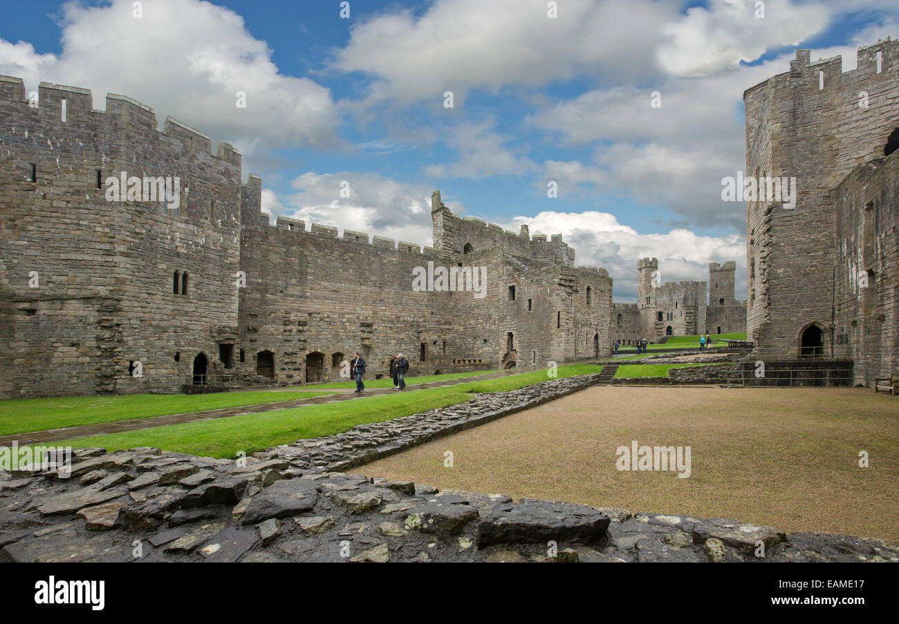 Vast spectacular interior of 13th century Caernarfon castle with huge walls & high towers around grassy courtyard under blue sky Stock Photo
