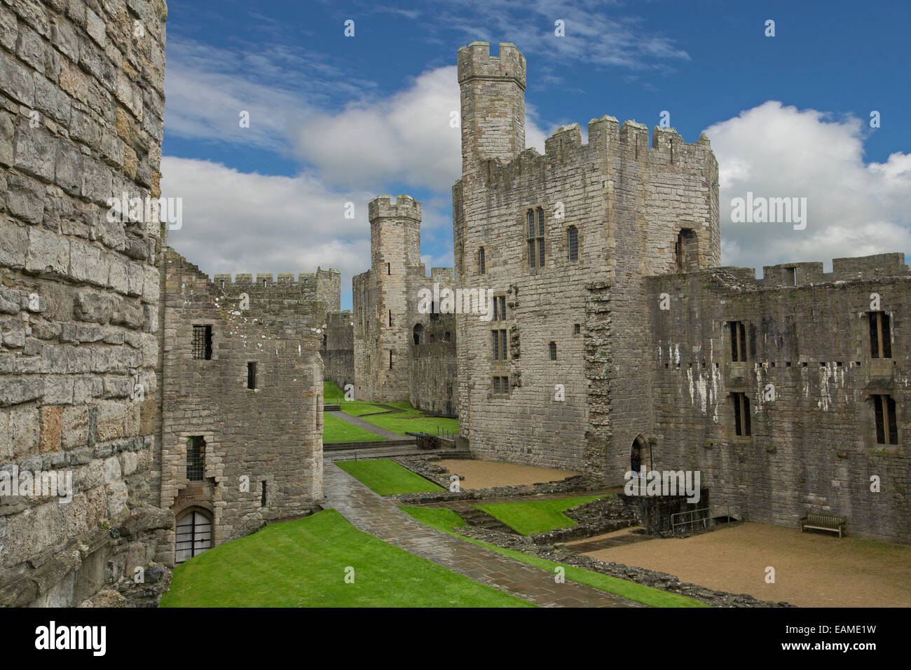 Spectacular interior of 13th century Caernarfon castle with huge walls & high towers around grassy courtyard under blue sky Stock Photo