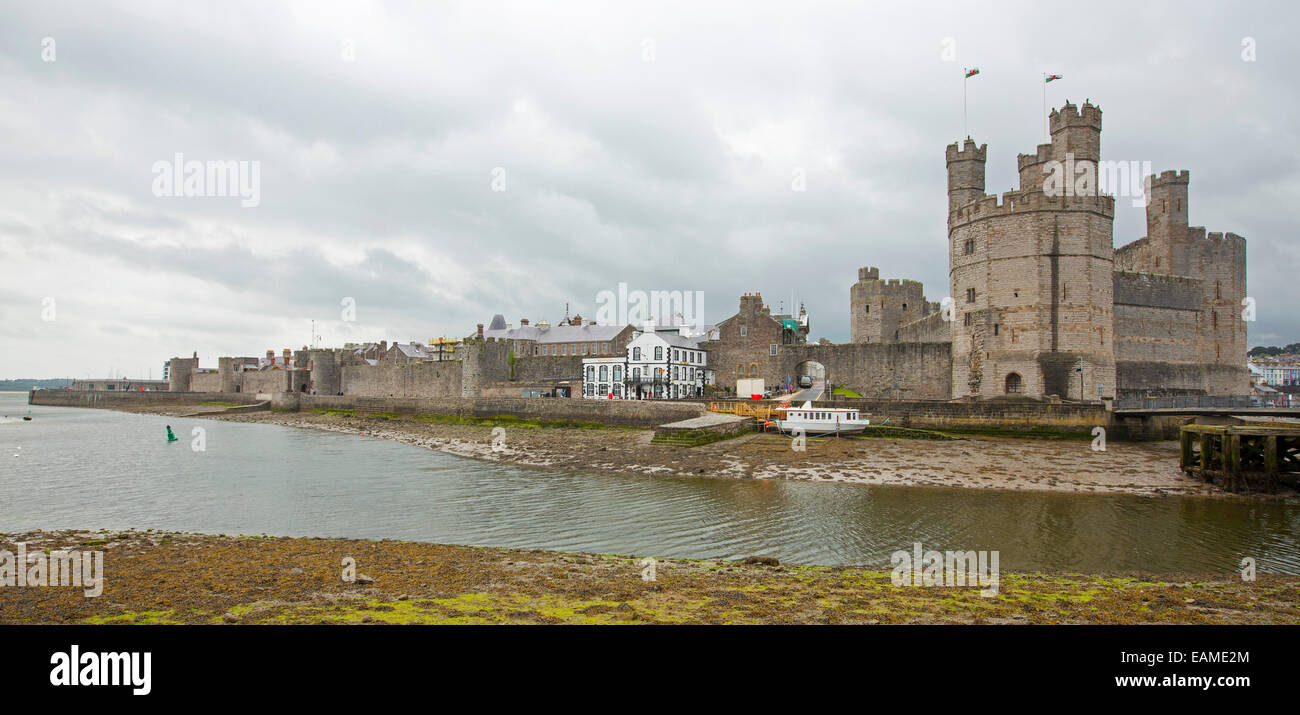 Panoramic view of spectacular Caernarfon castle towering over River Seiont with immense towers spearing into stormy sky in Wales Stock Photo
