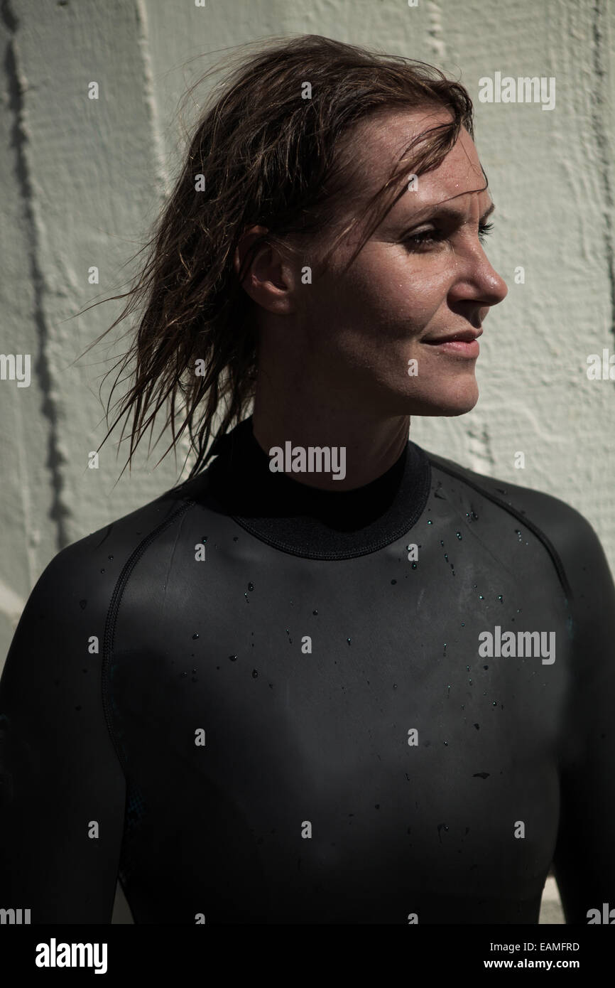 Attractive brunette female swimmer wearing black wetsuit with wet hair and looking calmly with slight smile and sunlight in face Stock Photo