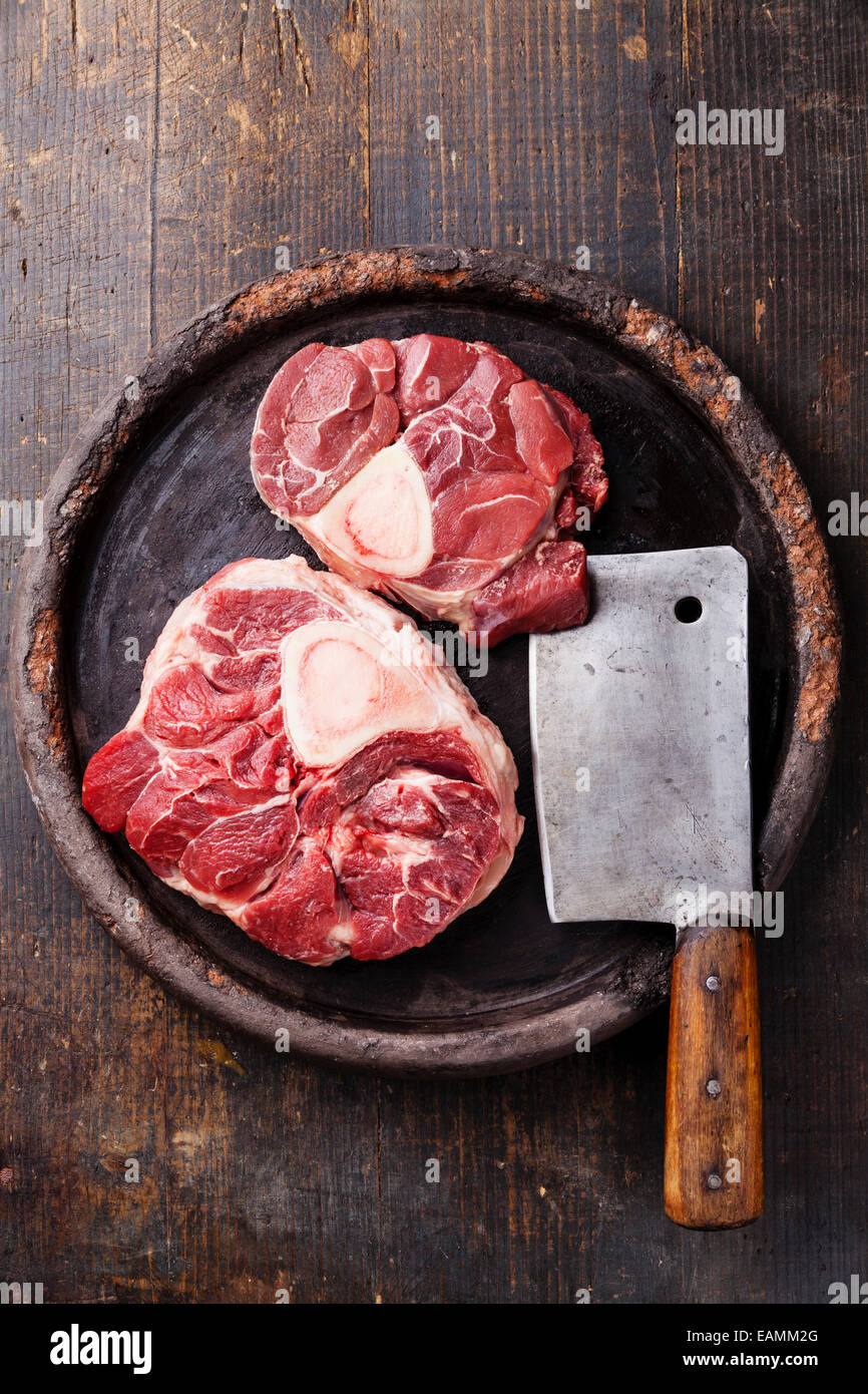 Raw fresh cross cut veal shank and meat cleaver for making Osso Buco on dark wooden background Stock Photo
