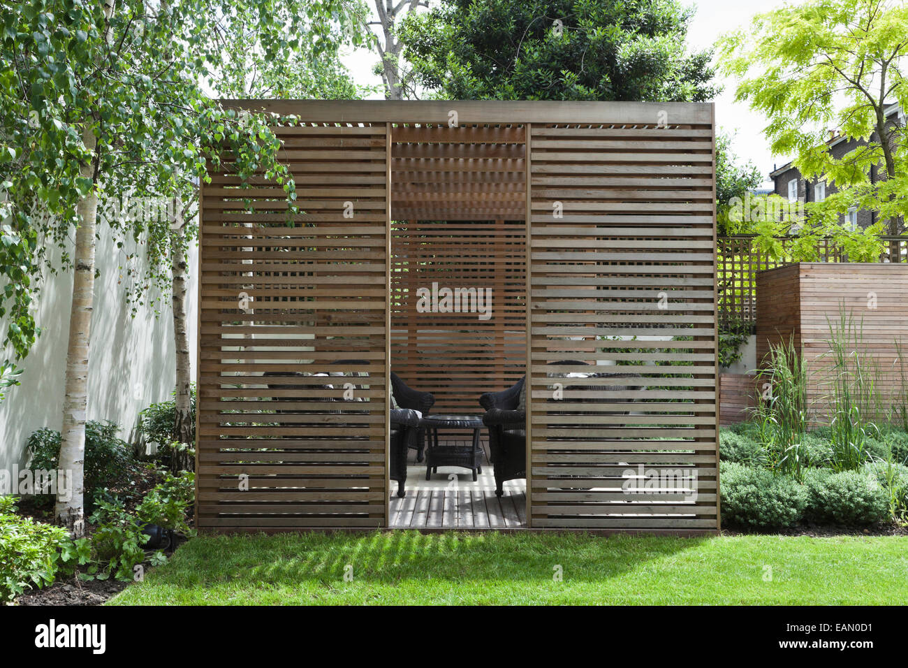 Slatted cedar pavilion on the right side of the lawn on the upper level of the garden, Silver birches along the boundary wall on the left Stock Photo