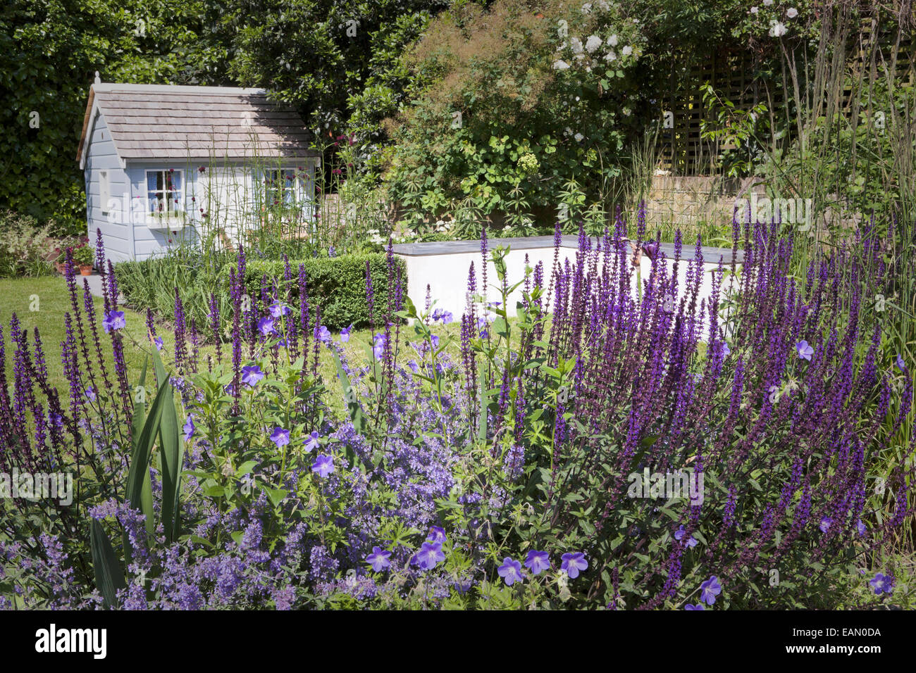 Raised bed built in grey brick with purple planting with playhouse at rear of garden, London Stock Photo