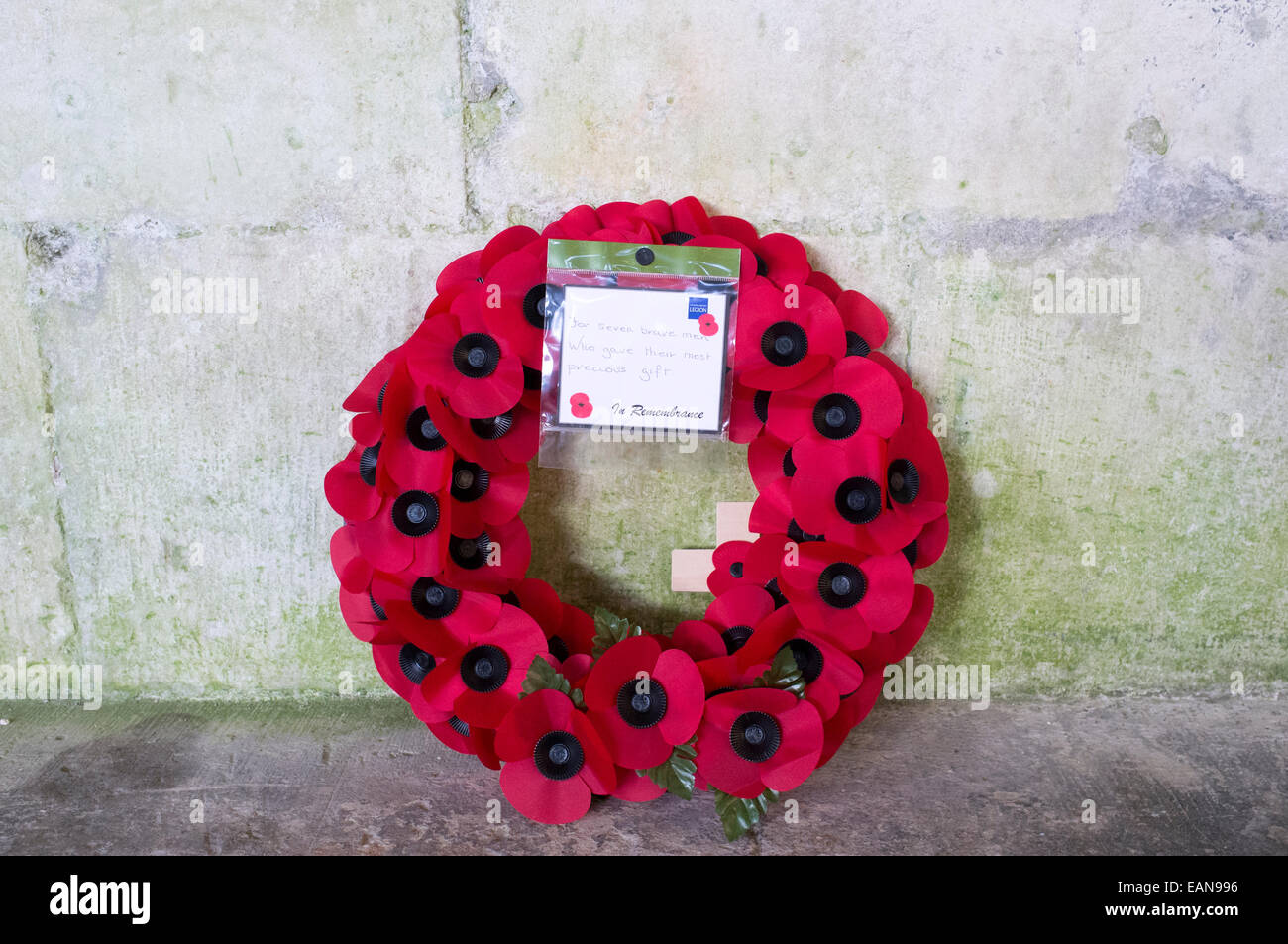 Poppy wreath leaning against stone wall with British Legion note of remembrance Stock Photo