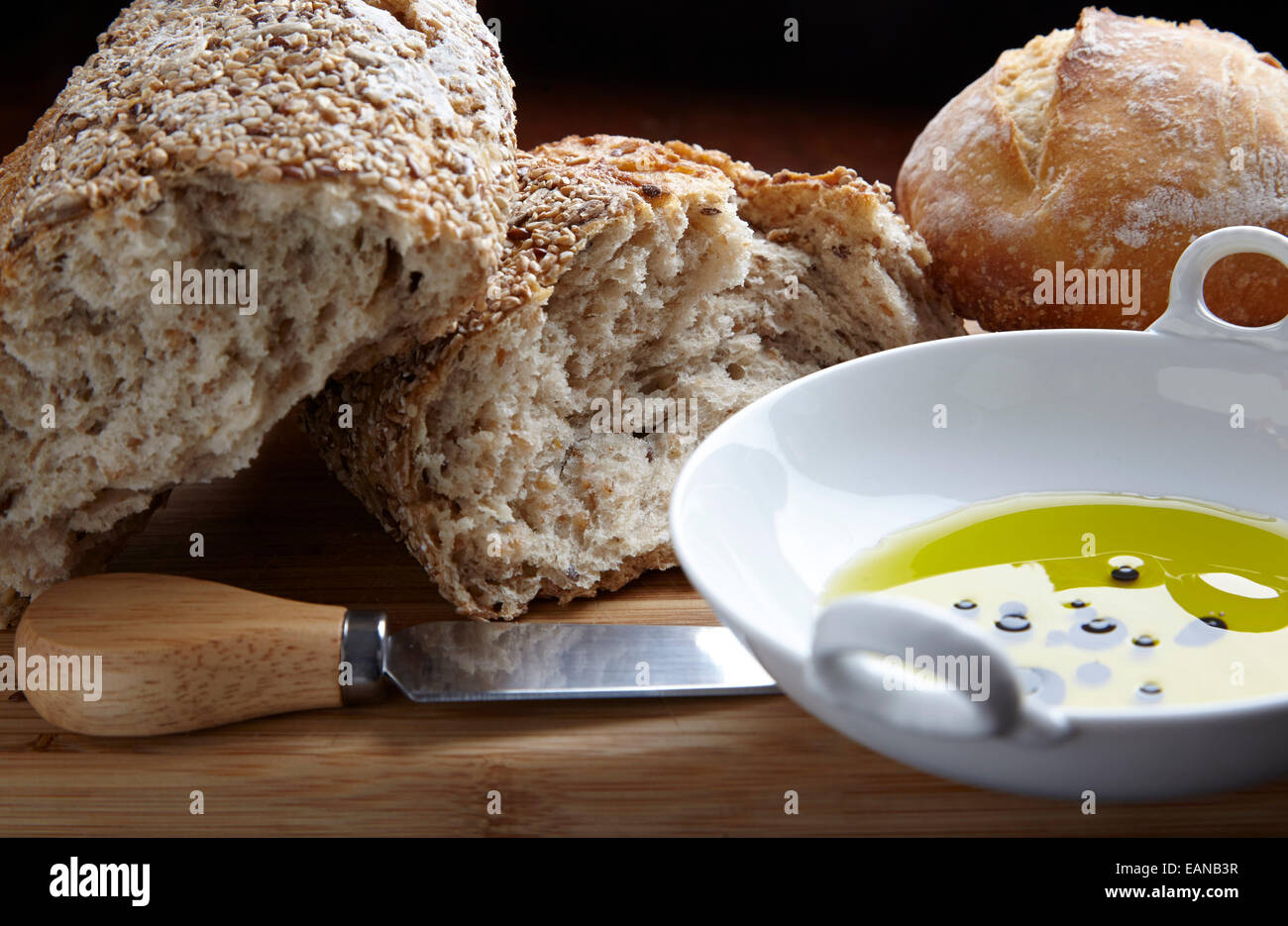 multi-grain bread with olive oil in a white bowl with a cutting knife on a wood board Stock Photo