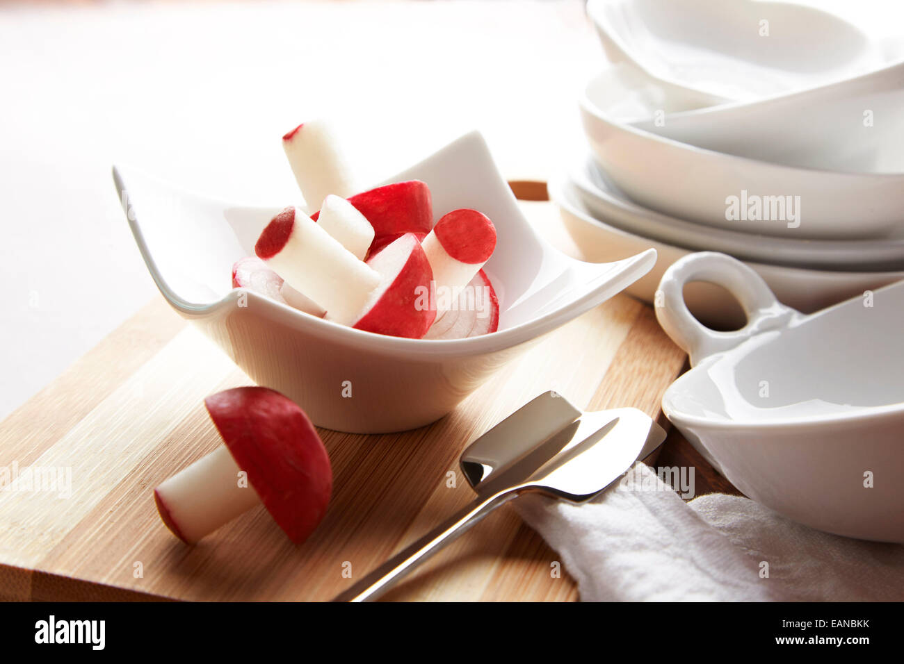 red decorative radishes in a white bowl with a silver cutter and a wood cutting board Stock Photo