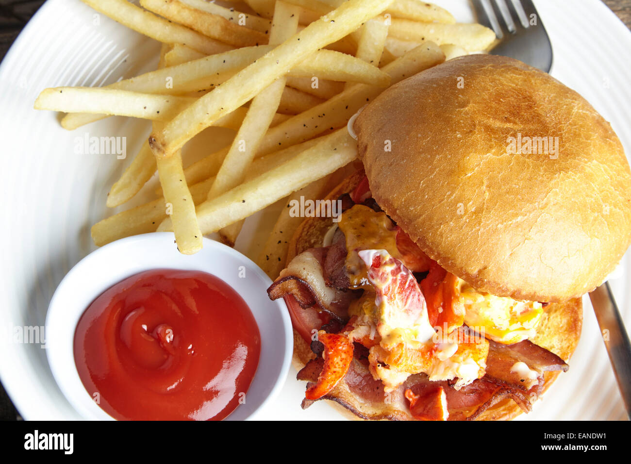 Main Lobster BLT tomato mayo on a brioche roll on a white plate with catchup and french fries Stock Photo