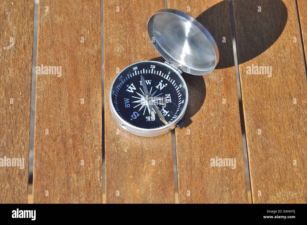 The compass on the boards. The magnetic compass lies on brown boards under the sun. Stock Photo