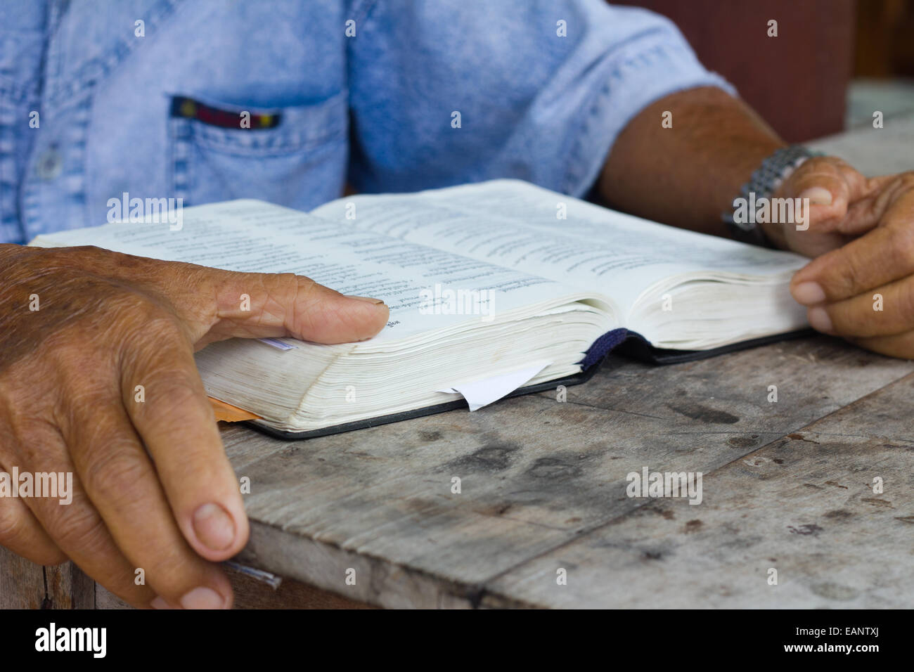 Thai old man reading bible on wooden table, focusing on bible Stock Photo
