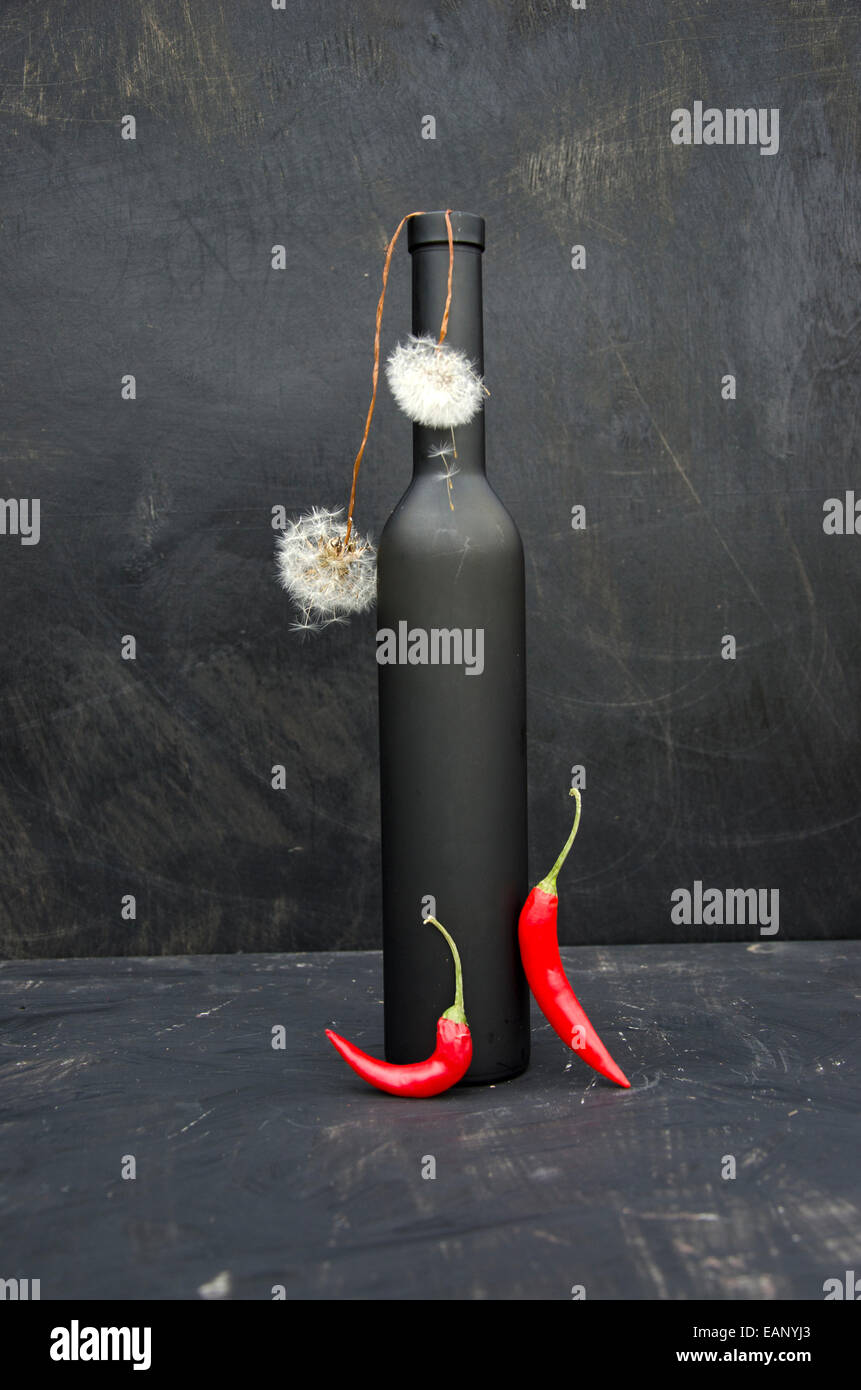 dark nature morte still-life with bottle, dandelion seeds and chili peppers Stock Photo