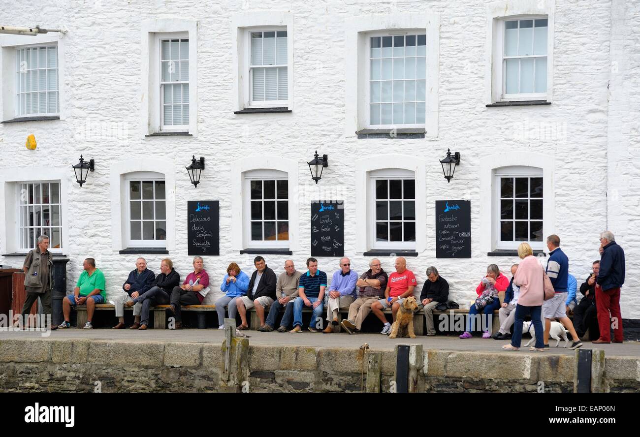 Holidaymakers sitting on a long bench in the Cornish fishing village of Mevagissey  England uk Stock Photo
