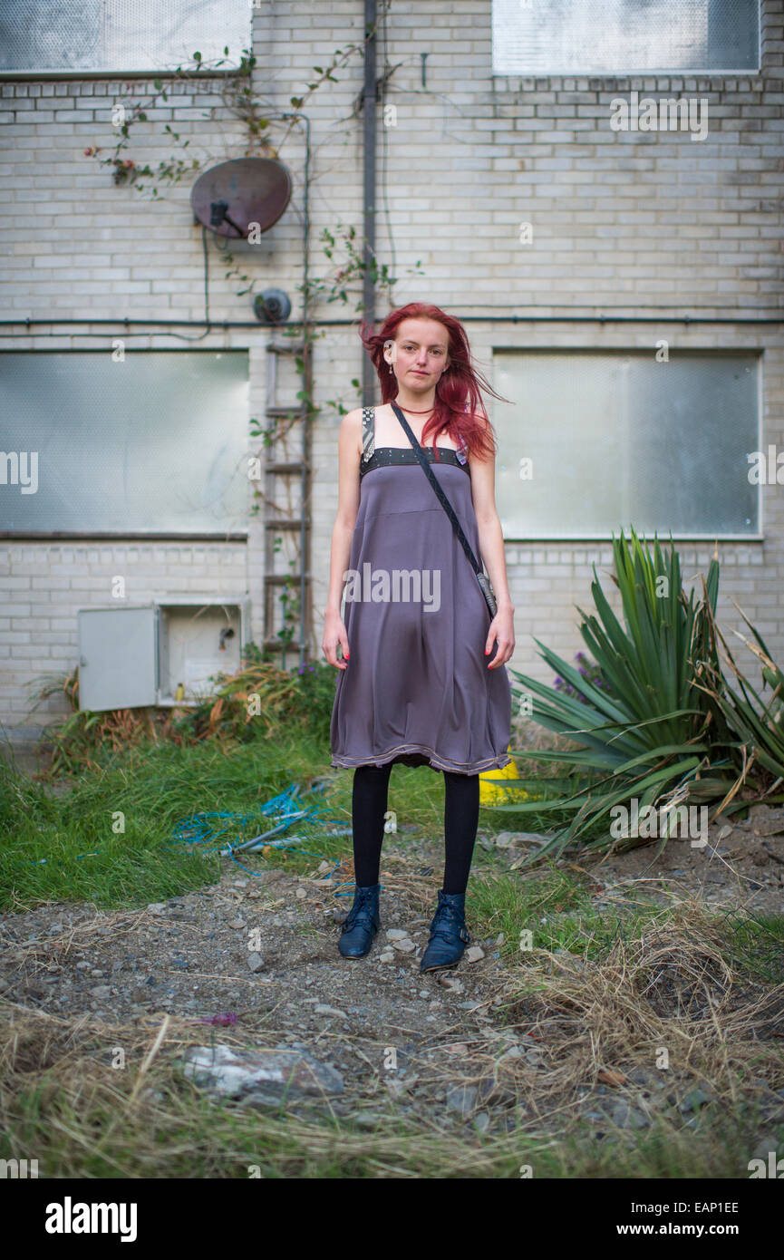 A slim thin tall Teenage girl young woman modeling wearing recycled  upcycled clothes clothing fashion outfit outdoors in a derelict grungy  run-down urban location outside an abandoned boarded up block of flats