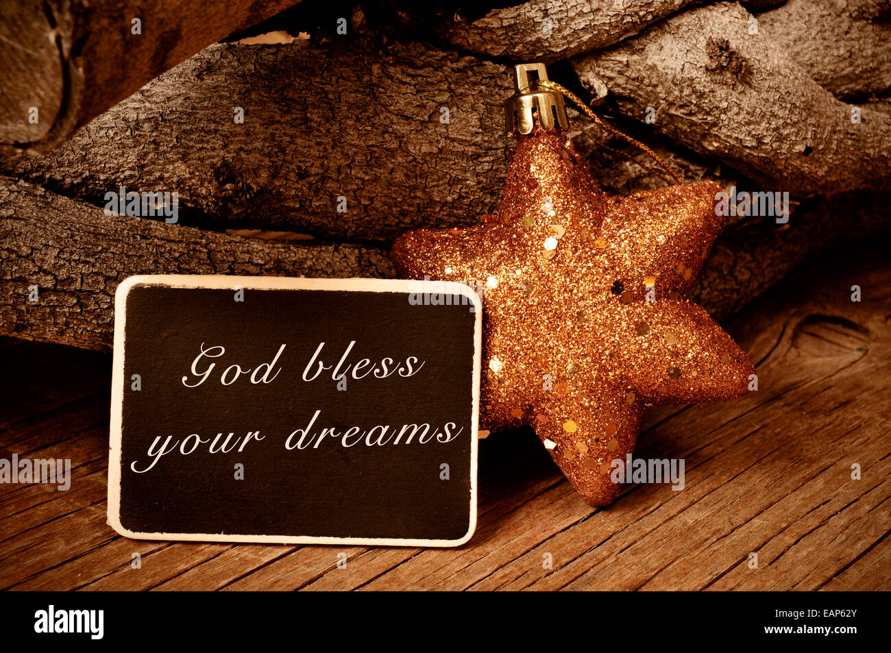 the text god bless your dreams written in a blackboard and a christmas star and a pile of logs in the background Stock Photo