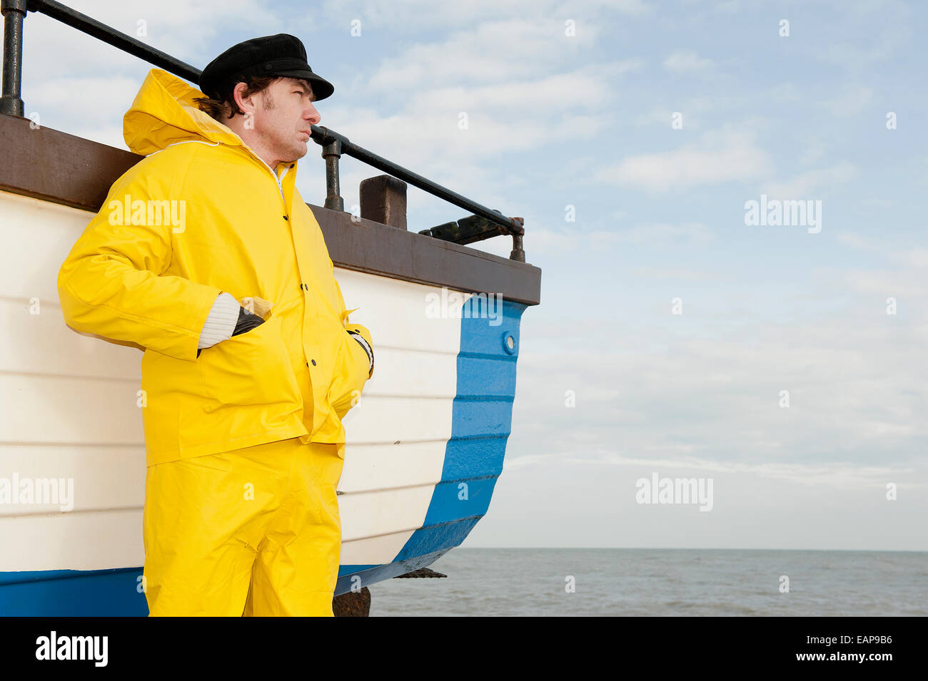 Sea fisherman in yellow waterproof overalls, standing by his fishing boat  and looking out to sea Stock Photo - Alamy