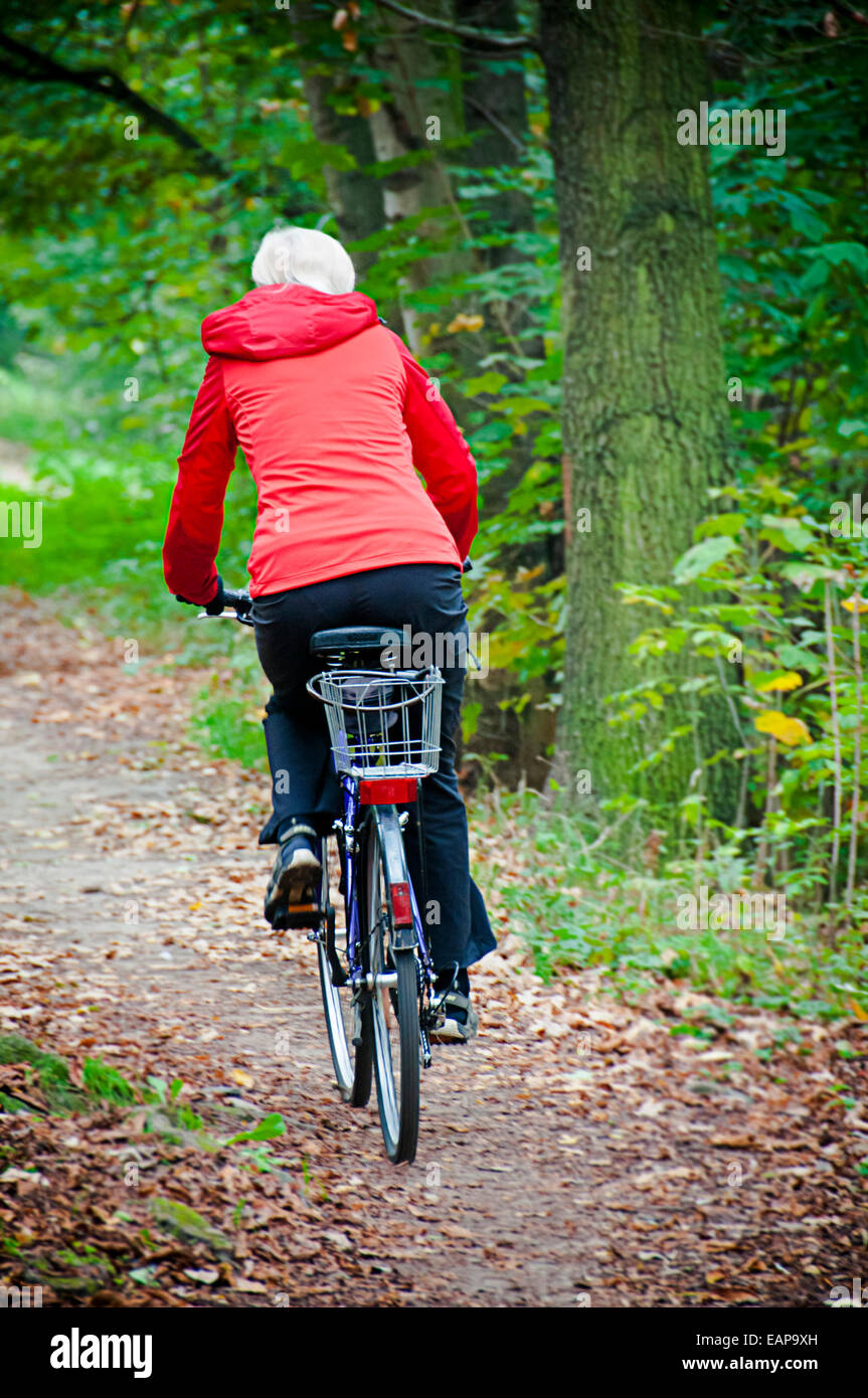 woman in red windbreaker riding a bicycle in nature Stock Photo