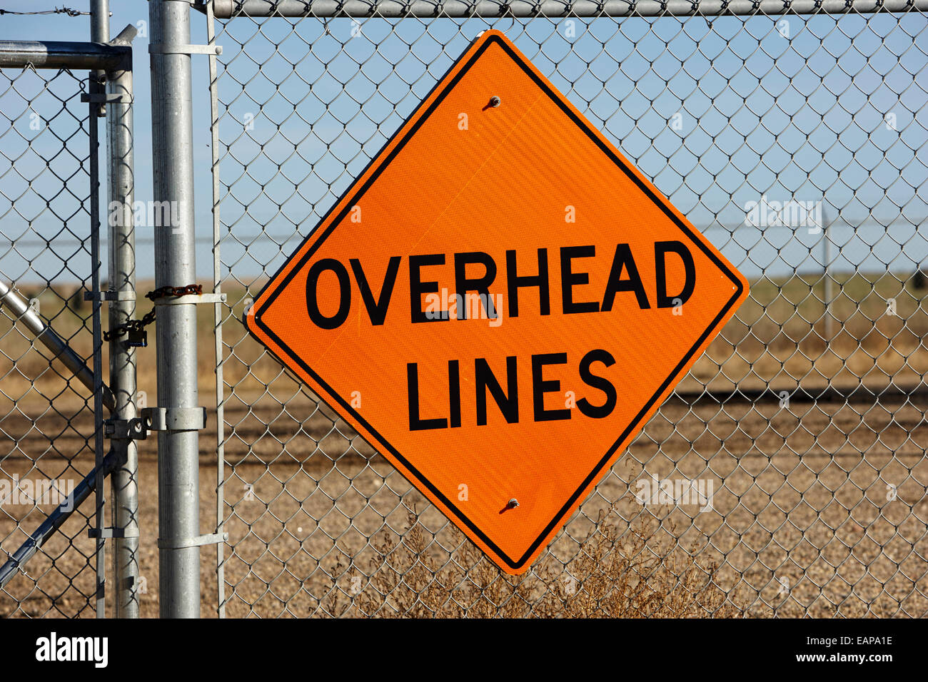 orange warning sign for overhead lines on a chain link fence Saskatchewan Canada Stock Photo