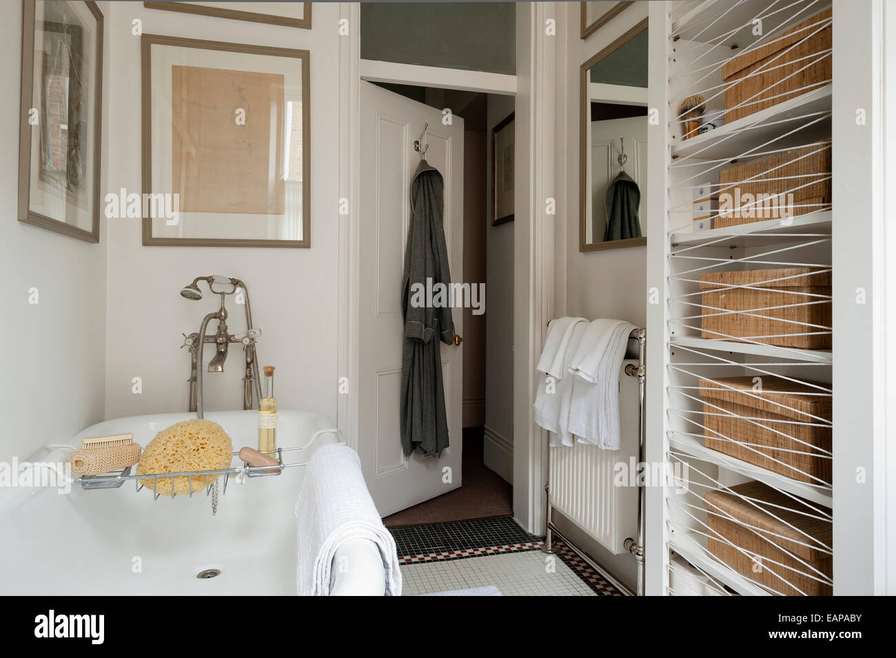 Antique prints and drawings on wall of bathroom with freestanding bath and tiled floor Stock Photo