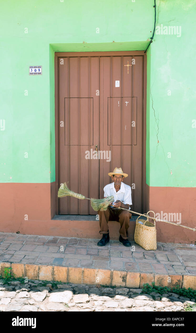 TRINIDAD, CUBA - MAY 8, 2014: An old broom street vendor seated at the door of a house Stock Photo