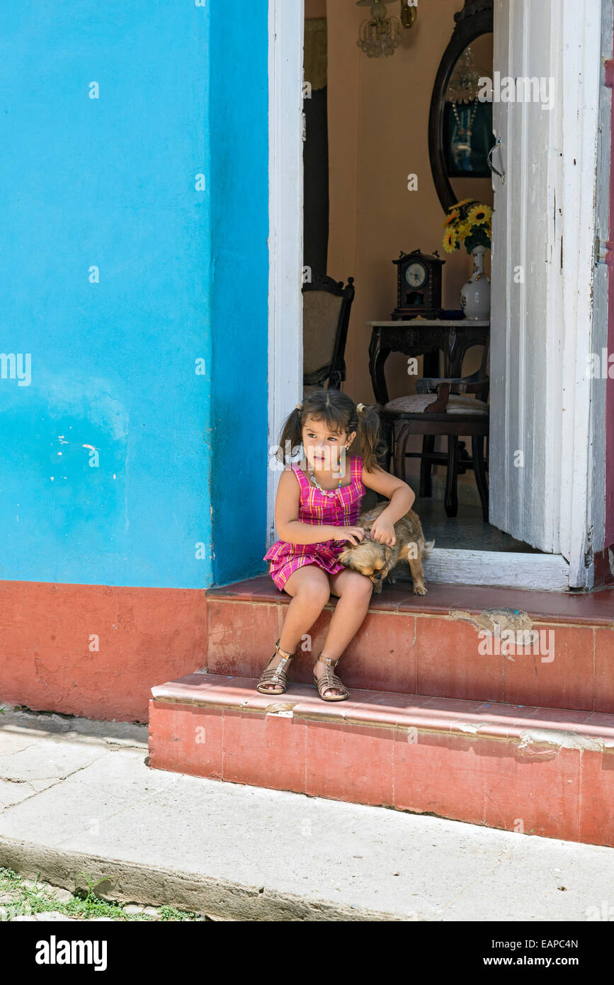 TRINIDAD, CUBA - MAY 8, 2014: Little girl plays with her dog sitting at your doorstep Stock Photo