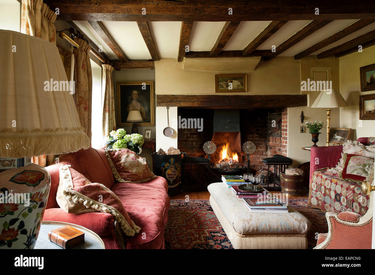 Inglenook fireplace in cosy sitting room with original beamed ceiling and red sofa Stock Photo