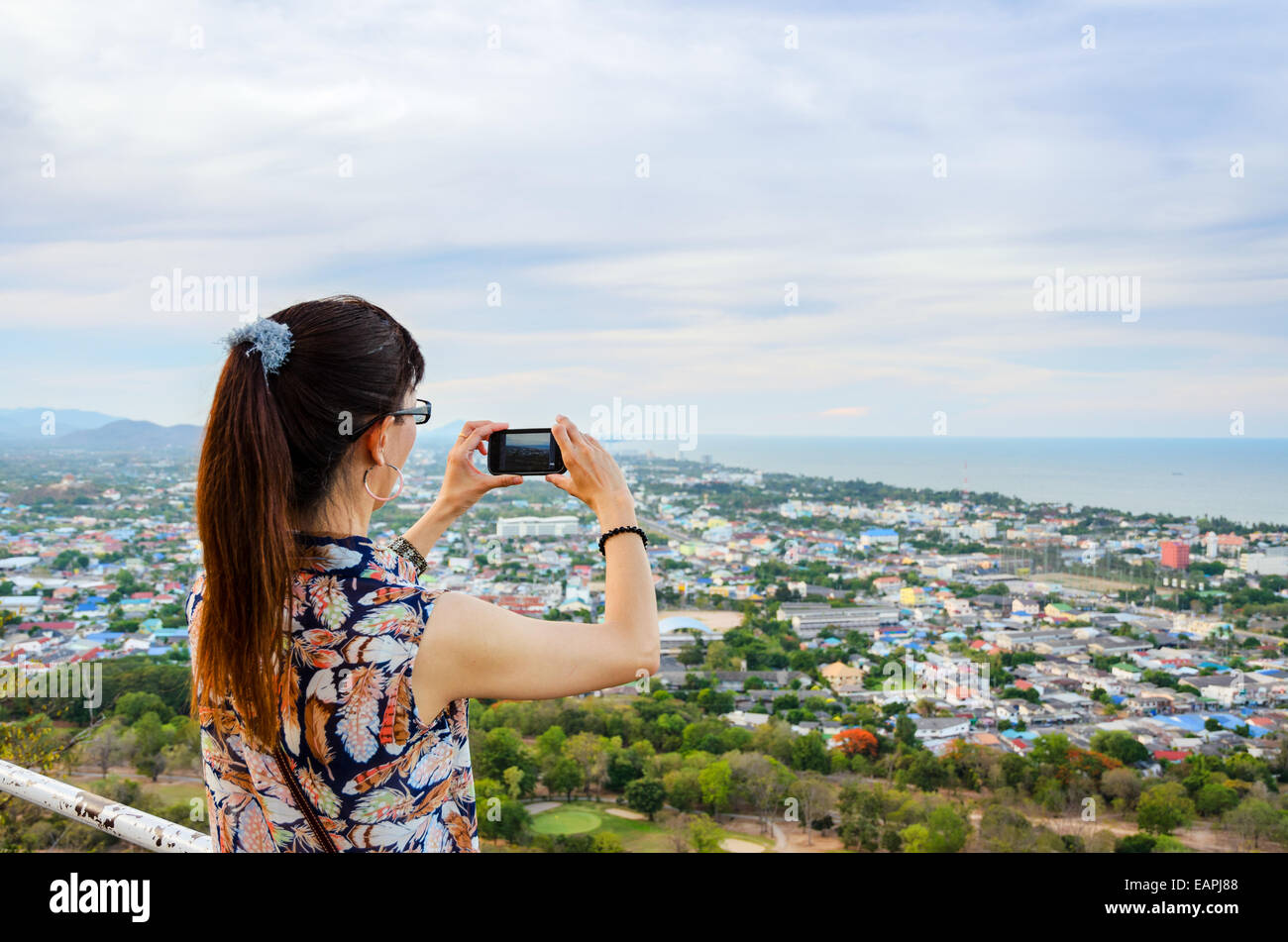 Woman using phone taking pictures of the Hua Hin city from on high. Thailand Stock Photo
