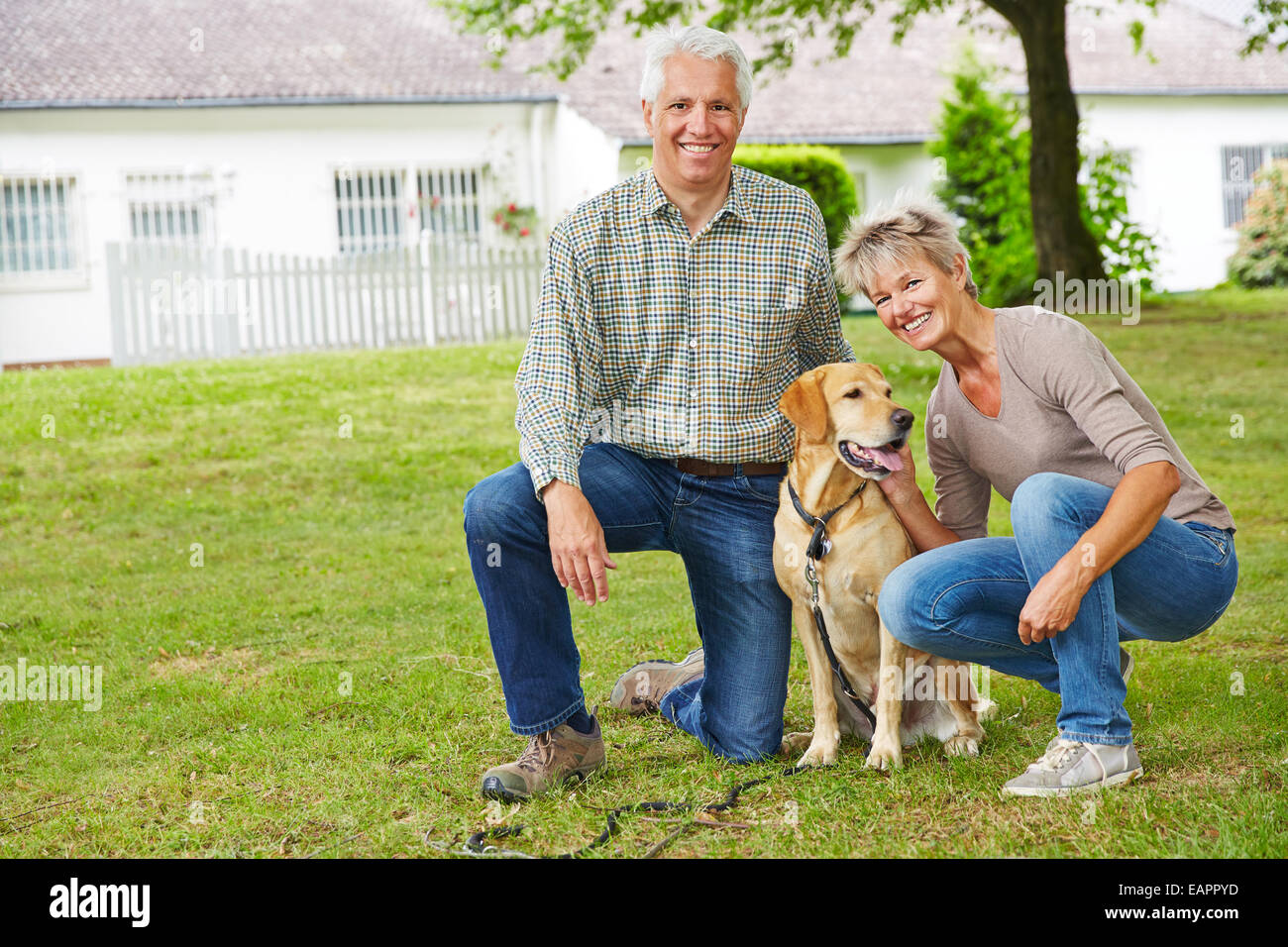 Two smiling senior people sitting with dog in front of their house in the garden Stock Photo