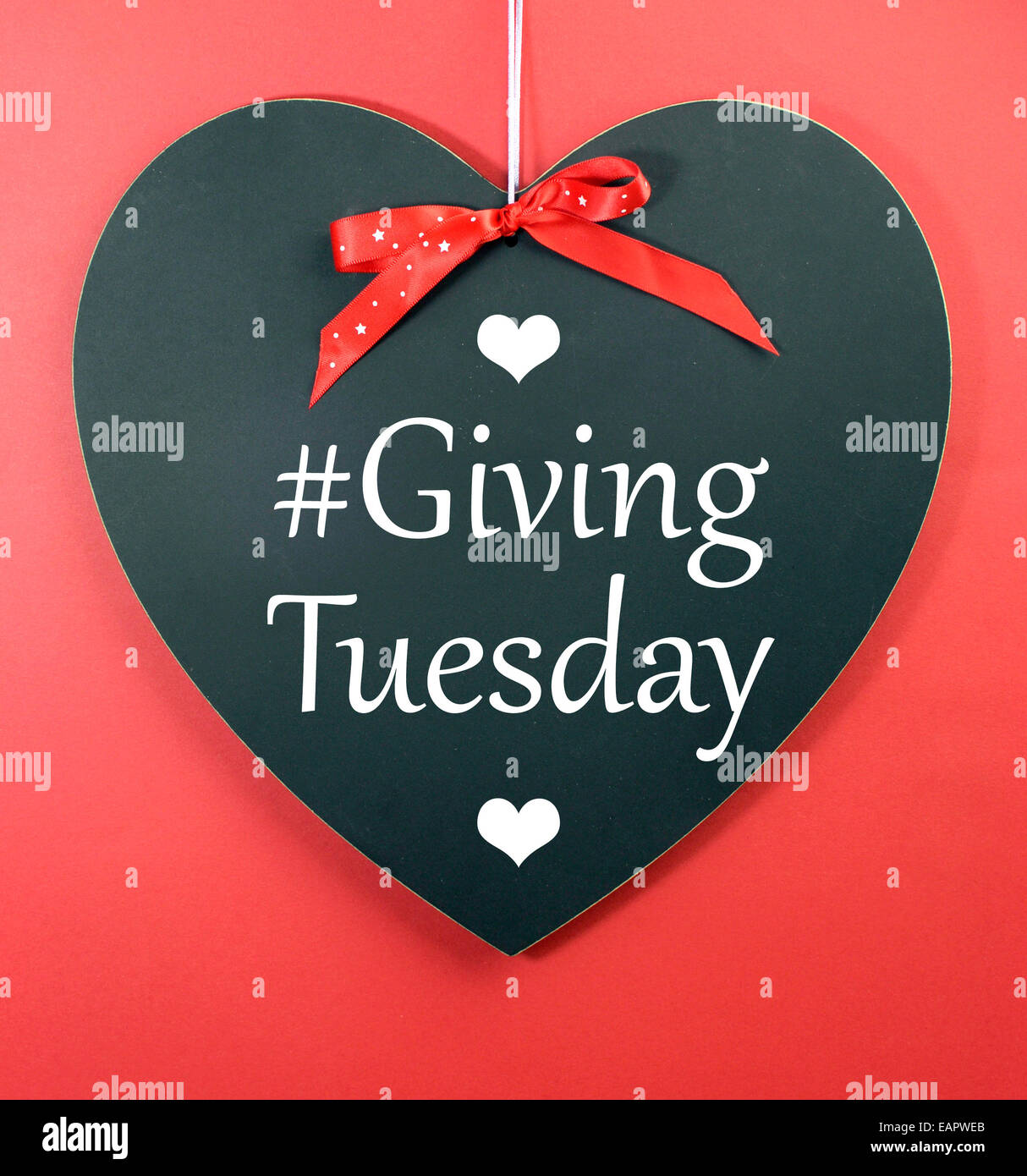 Giving Tuesday message greeting on black heart shape blackboard against a red background. Stock Photo