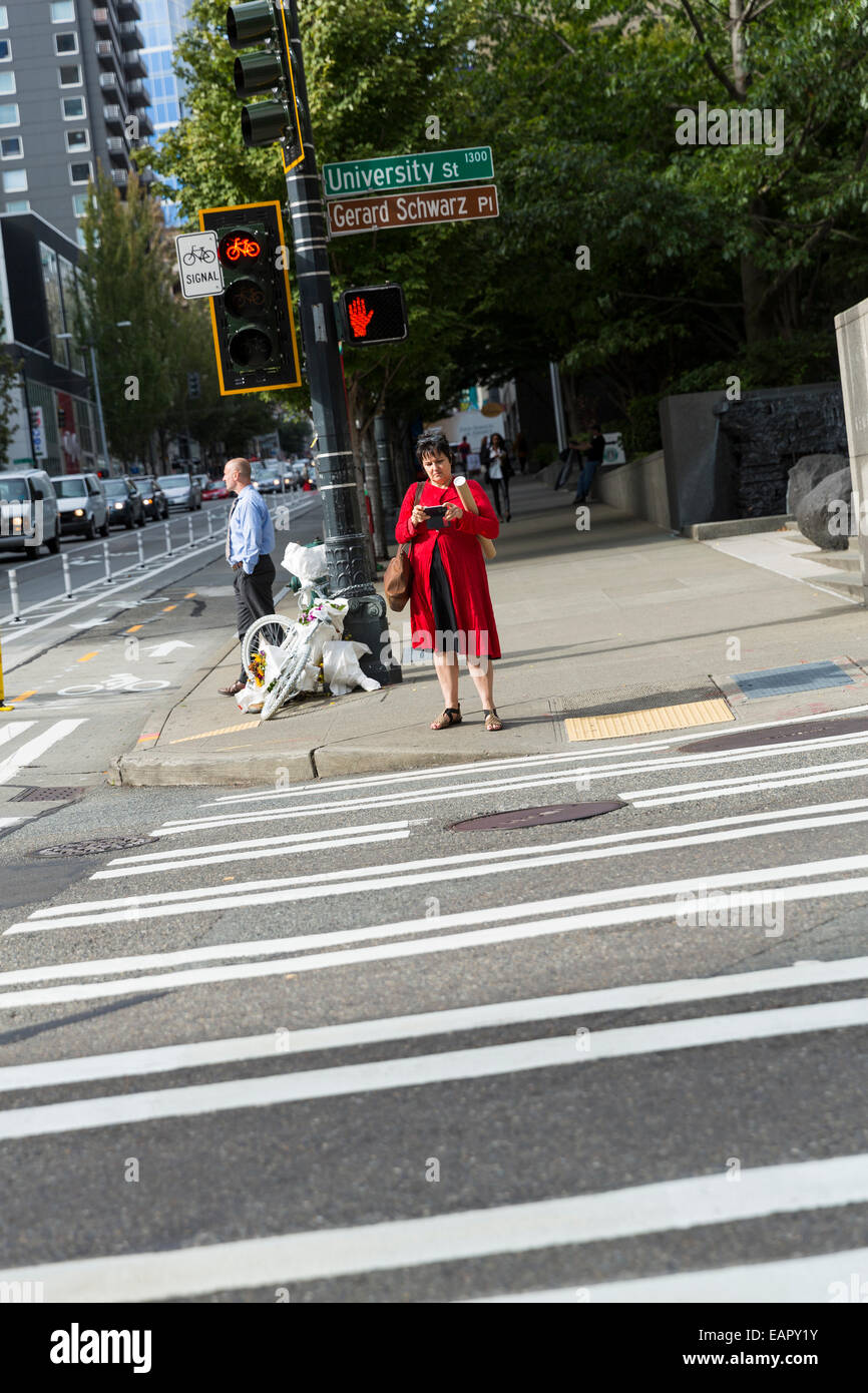 Woman in a red coat waiting for a green light to cross a street and looking on her phone Stock Photo