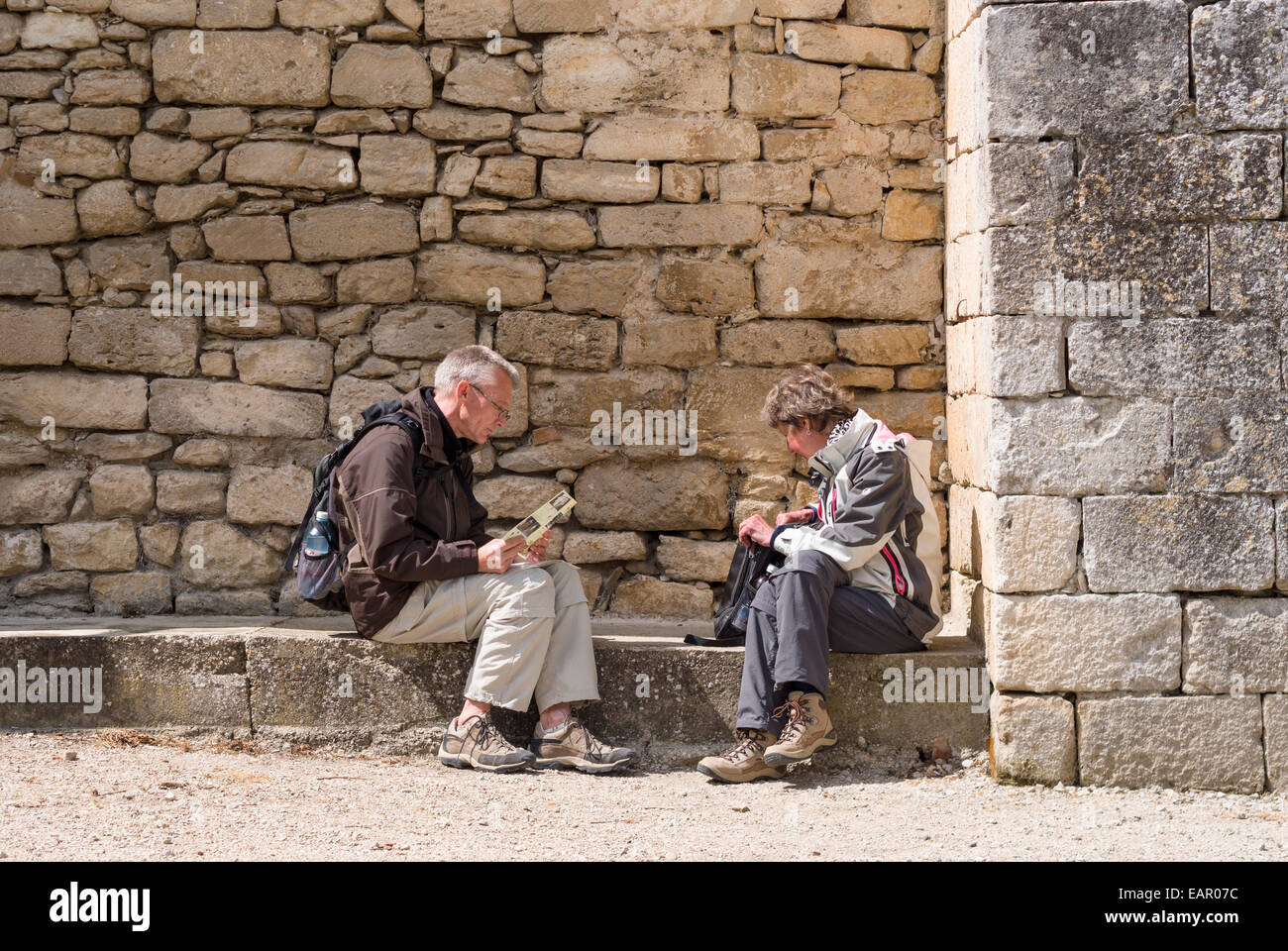 Taking a Break from Touring. Two middle aged tourists take a break on stone bench beneath asylum wall and check a brochure Stock Photo