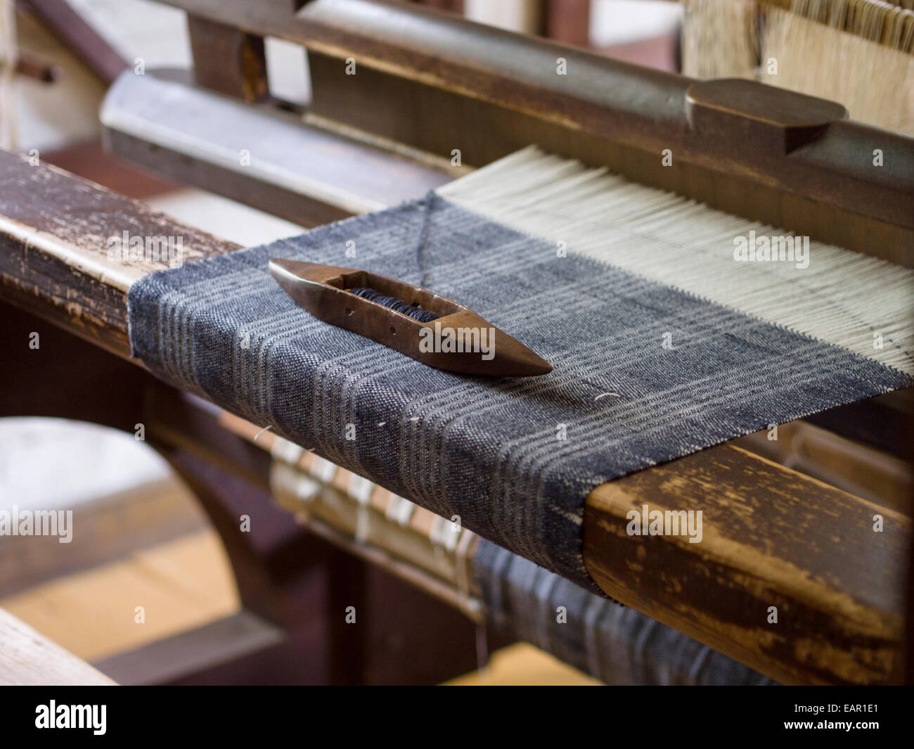 Shuttlecock on a Tartan Weave. A shuttlecock with blue wool rests on a Tartan piece of cloth being woven on a vintage home loom. Stock Photo