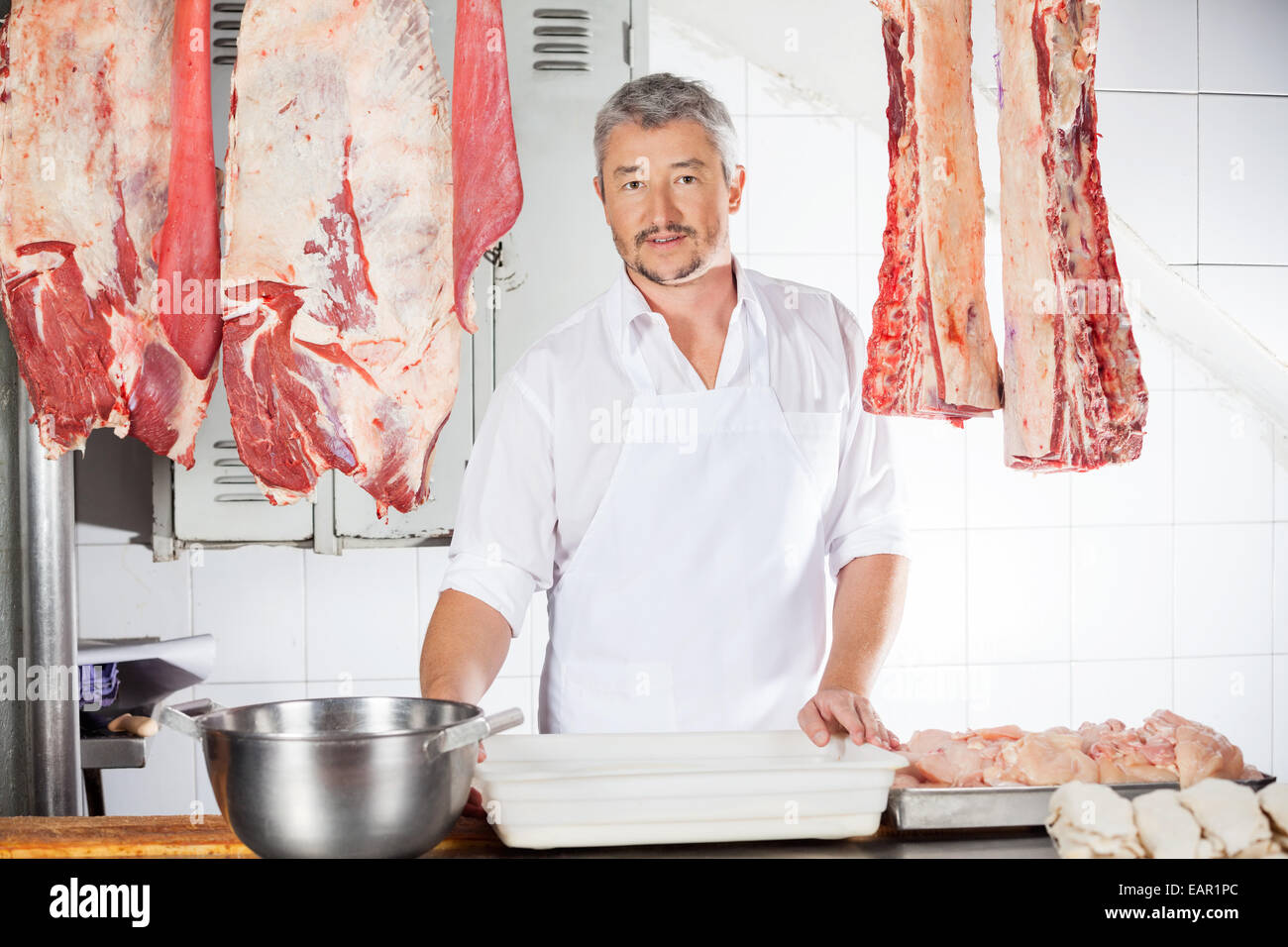 Butcher Amidst Meat Hanging In Shop Stock Photo Alamy