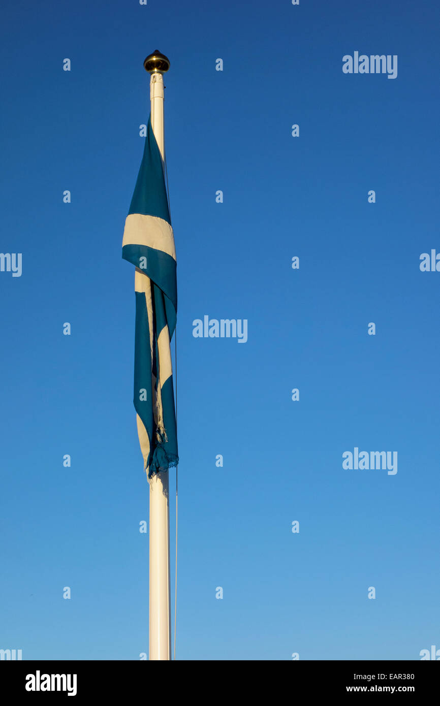 The Flag of Scotland, also known as Saint Andrew's Cross or the  Saltire, drooping on a white flag pole with a blue sky behind Stock Photo