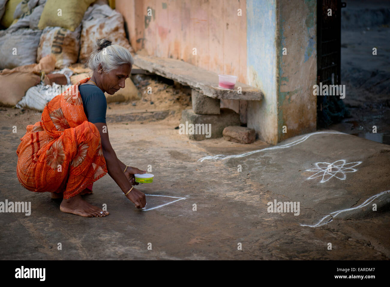 Elderly woman creating a traditional Rangoli, Kolam or Muggu, decorative pattern made of coloured sand, outside a door Stock Photo