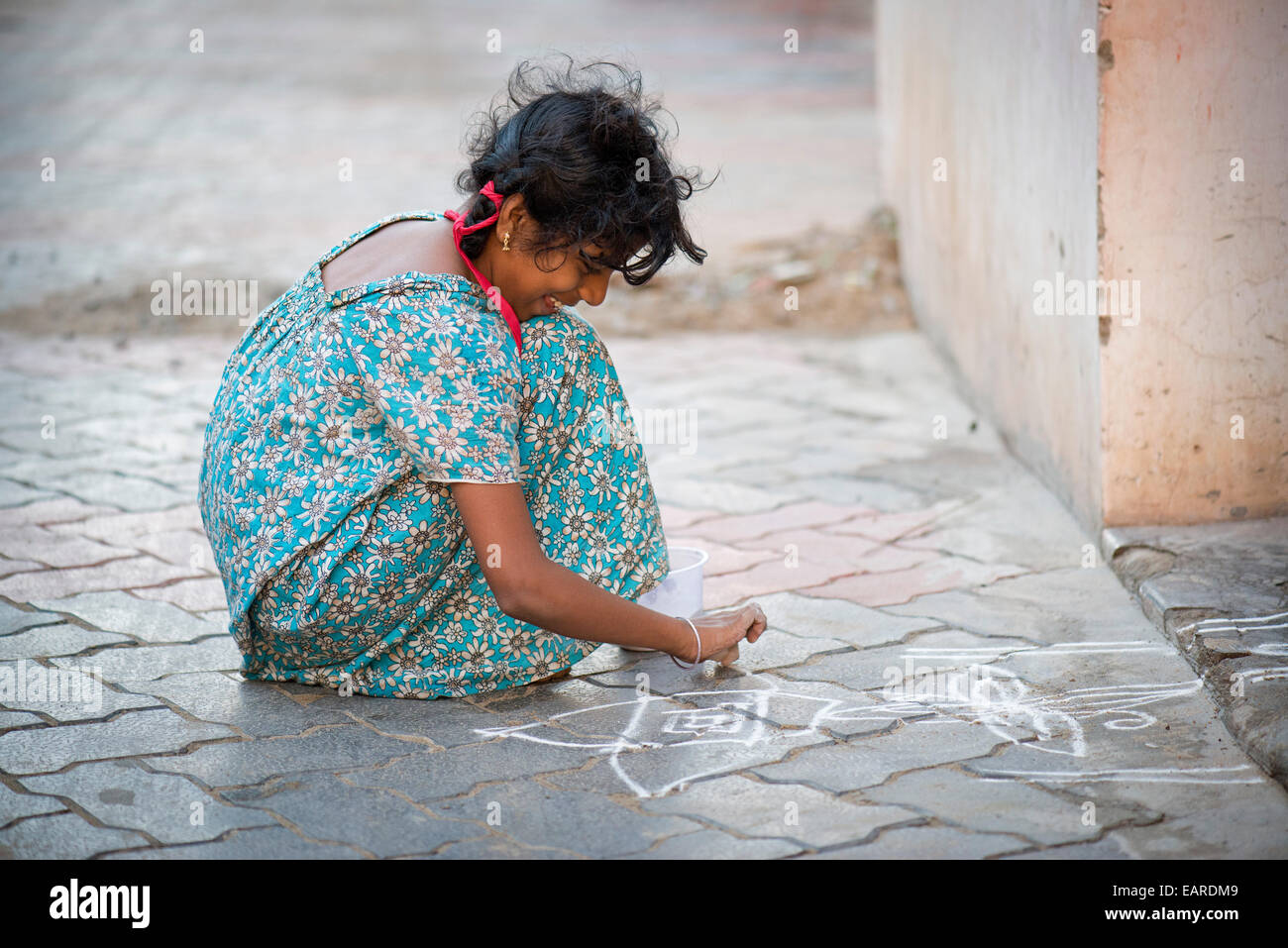 Girl creating a traditional Rangoli, Kolam or Muggu, decorative pattern made of coloured sand, outside a door, Rameswaram Stock Photo