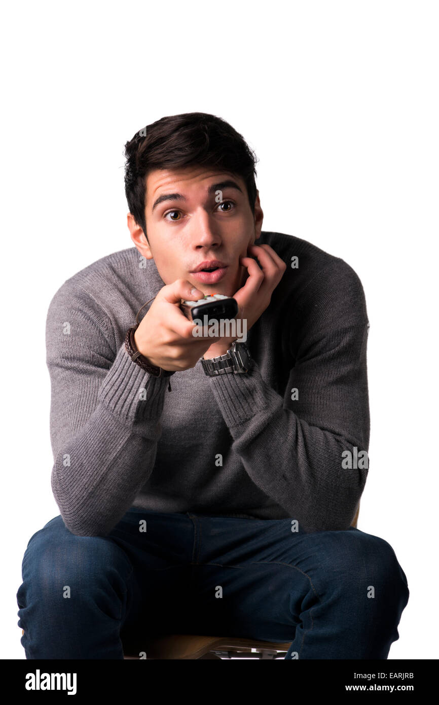 Handsome young man holding remote control and changing TV channels, sitting isolated on white Stock Photo
