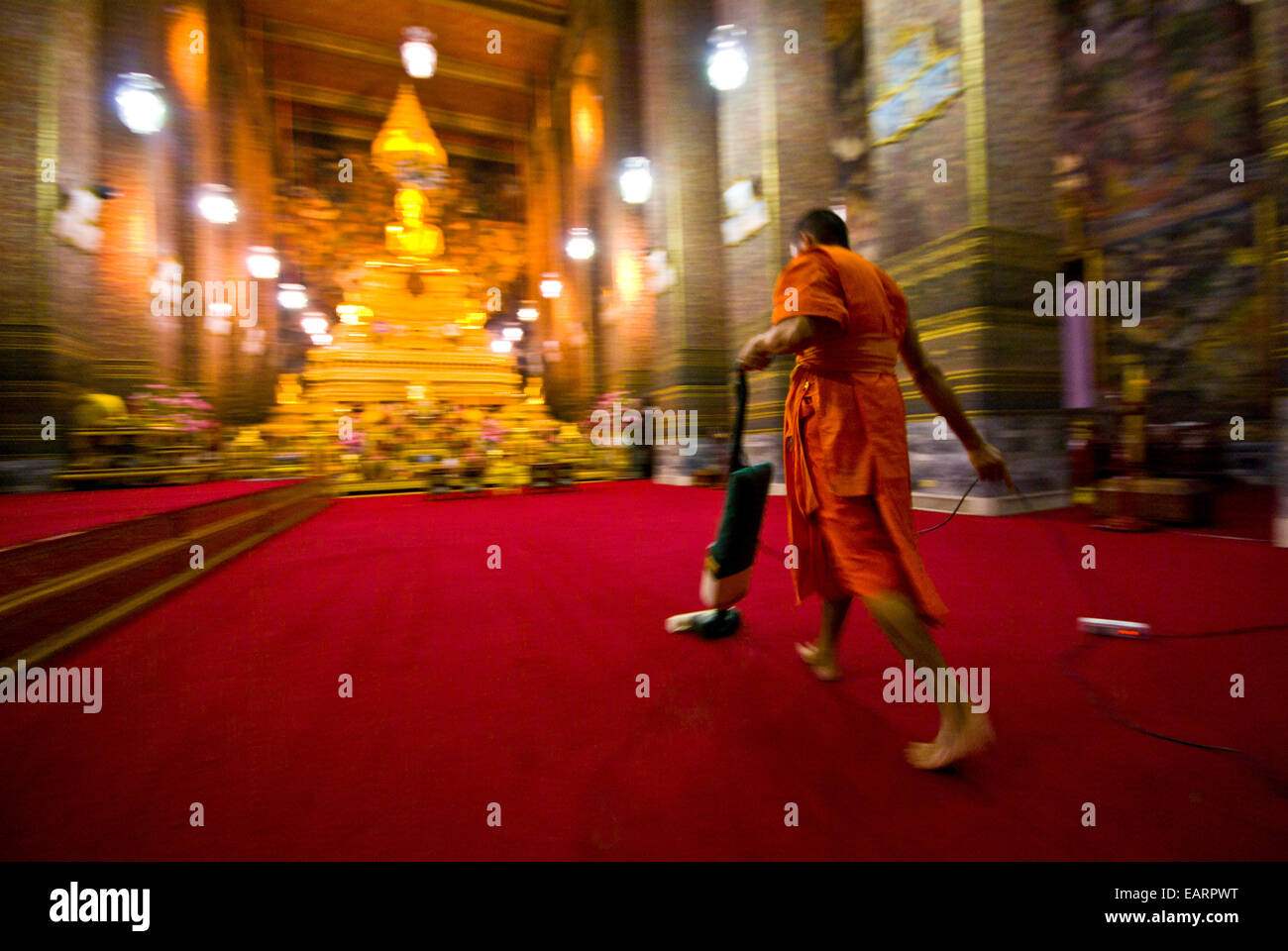 A Buddhist Monk vacuums the chapel's red carpet after evening prayer. Stock Photo
