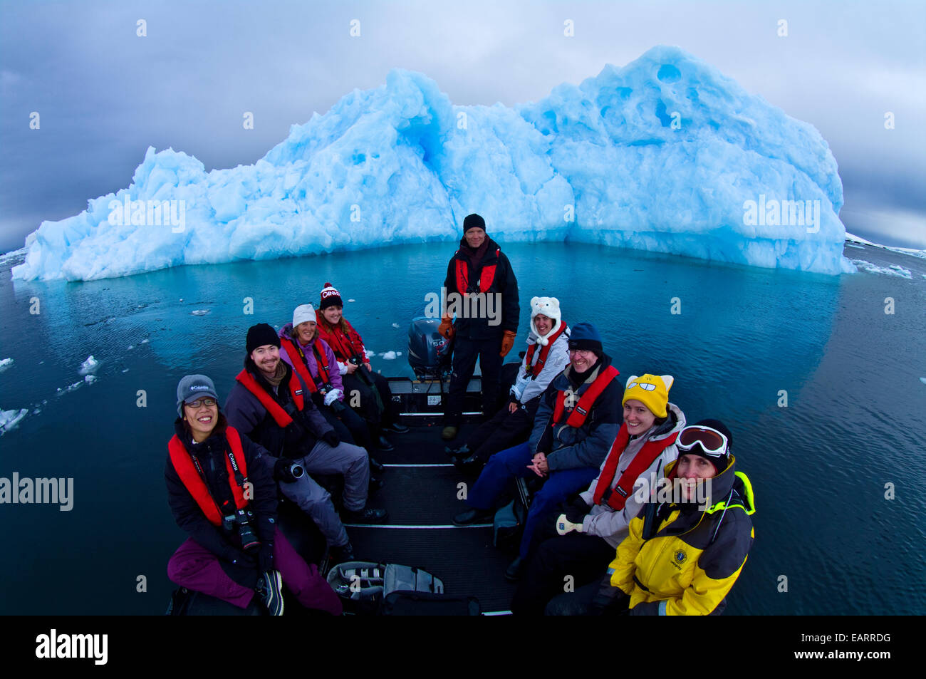 Tourists in a boat pose in front of a jagged blue Antarctic iceberg. Stock Photo