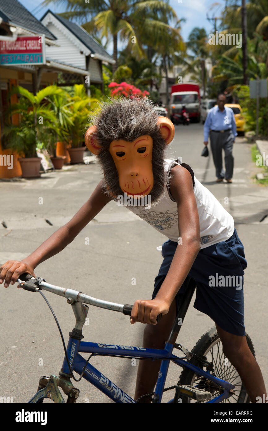 Mauritius, Grand Baie, child wearing monkey mask whilst riding bicycle Stock Photo