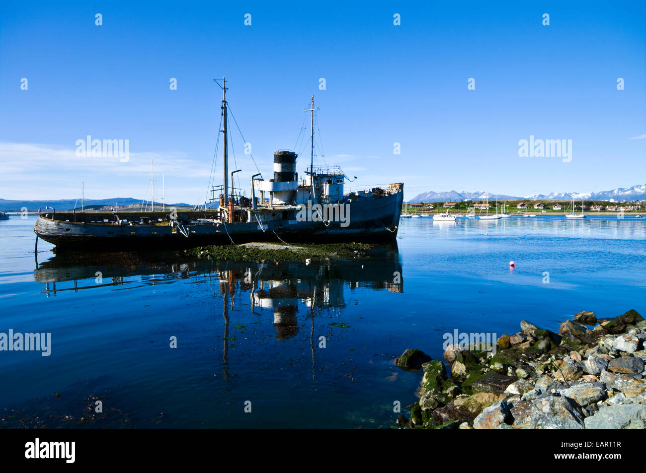 A tugboat shipwreck rests in the shallows of a sheltered bay. Stock Photo