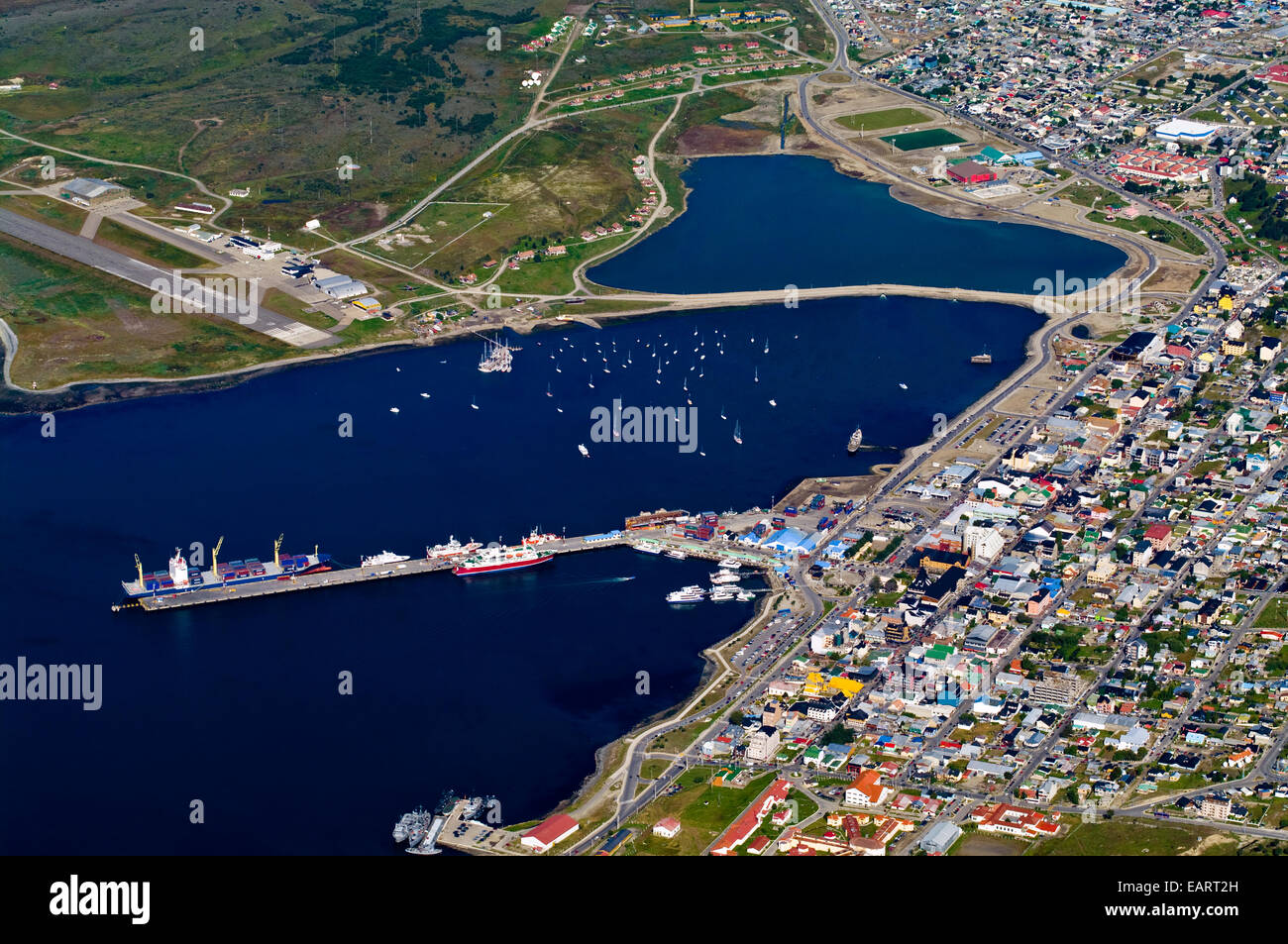 Container ships at wharf and yachts in a sheltered harbor by a city. Stock Photo