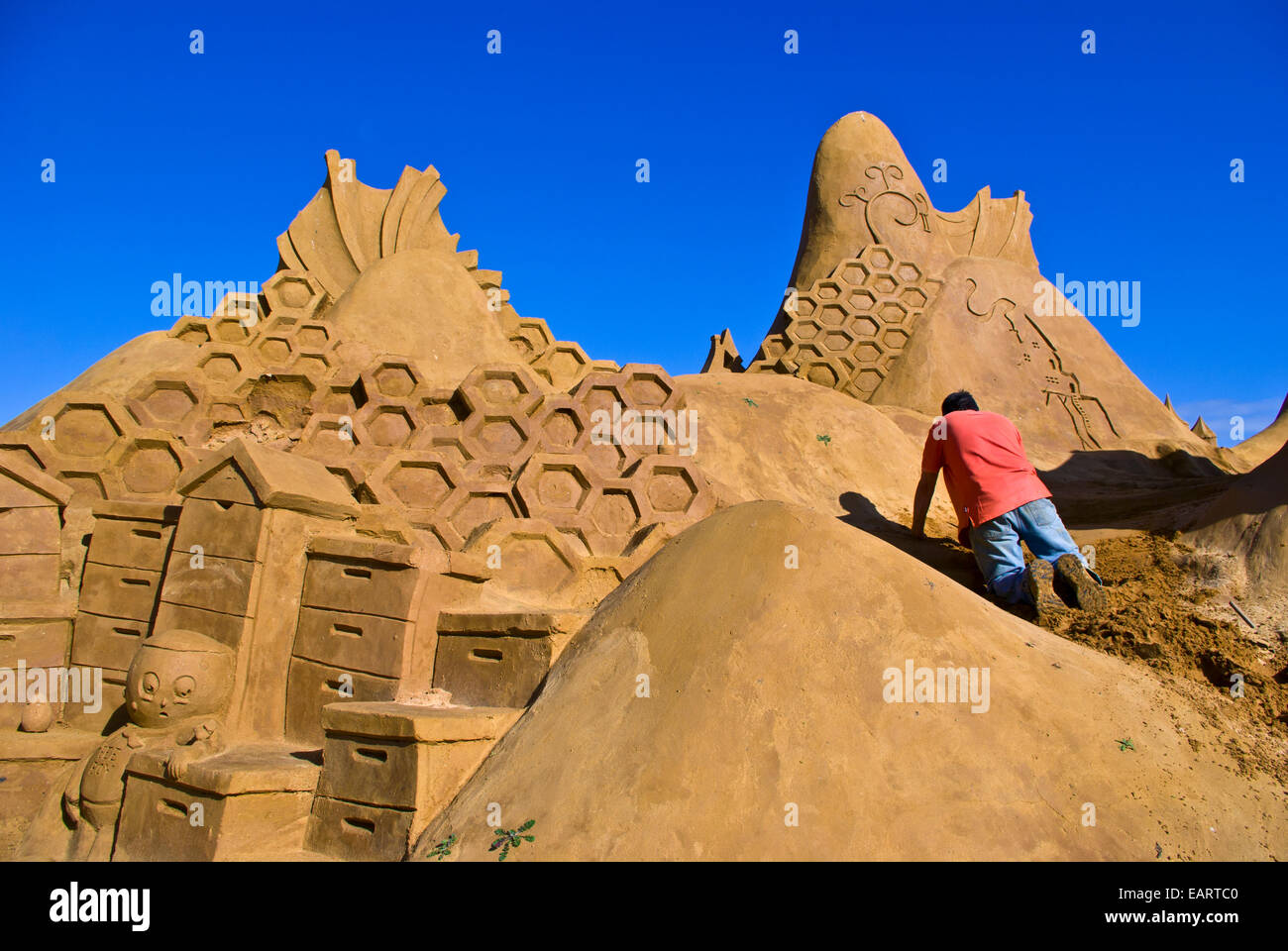 A professional sand sculptor carves a bee hive honeycomb sculpture. Stock Photo