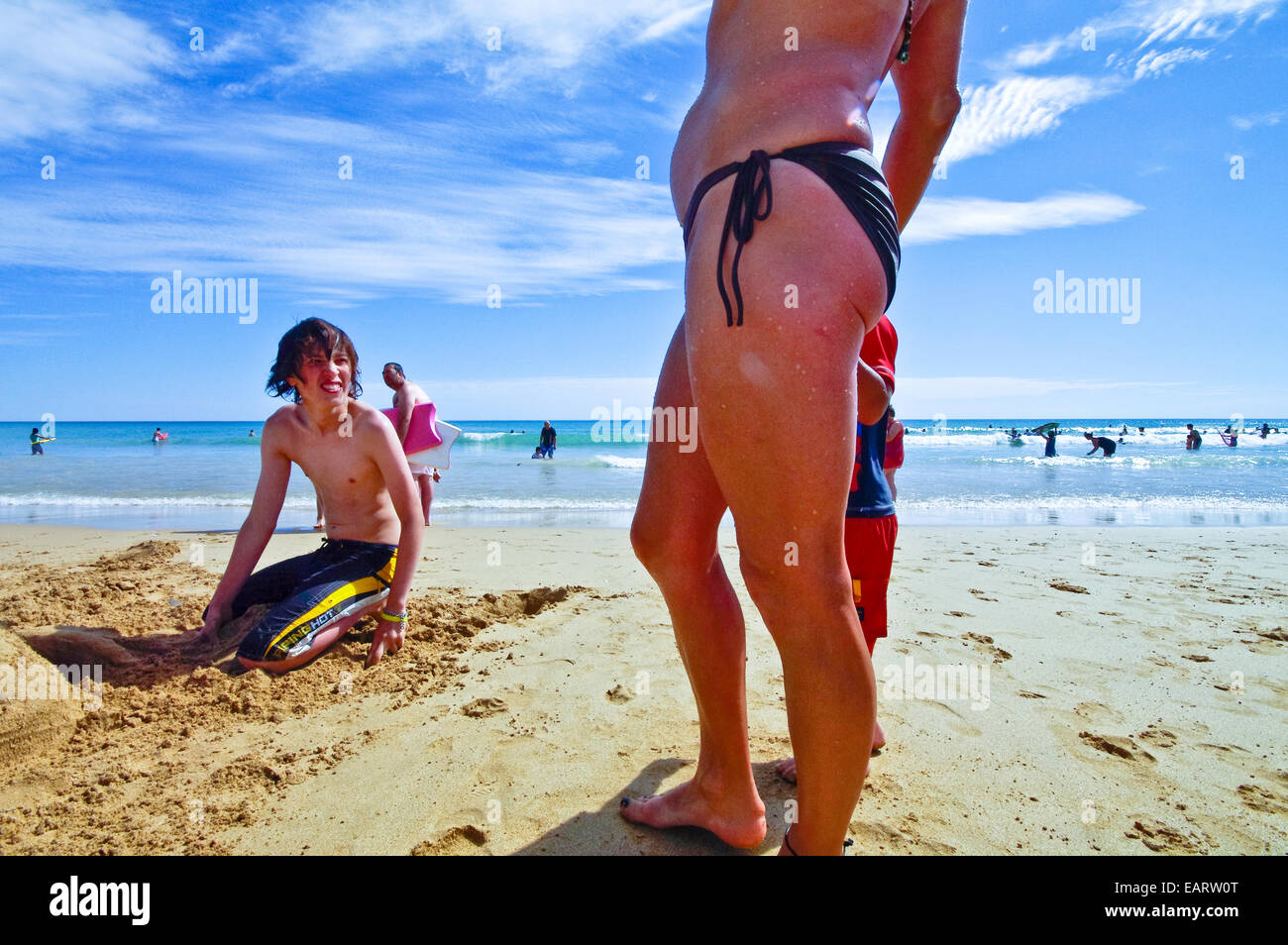 Young beautiful fit sporty female model pose in micro blue tight bikini by  standing on beach next to a sea Stock Photo